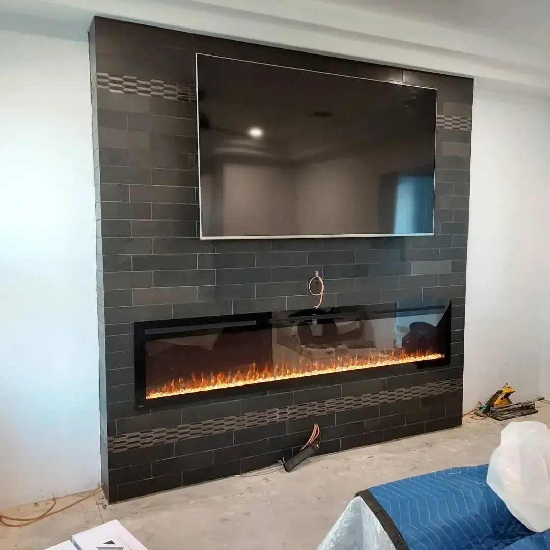 A fireplace and television setup: black tiled wall, electric fireplace below a large TV.