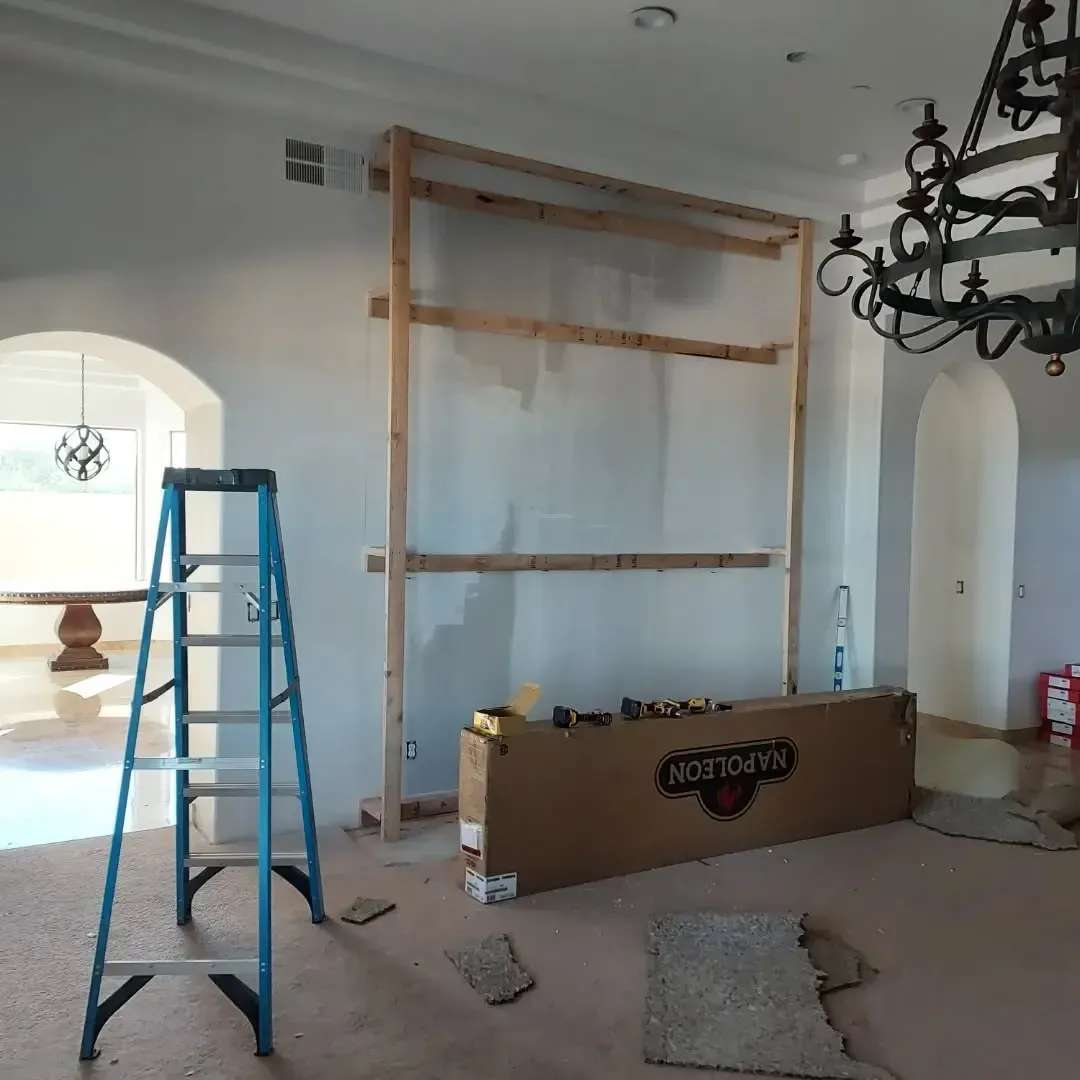 Interior renovation: A wooden frame with plastic sheeting stands against a wall. A ladder, box, and chandelier are visible.