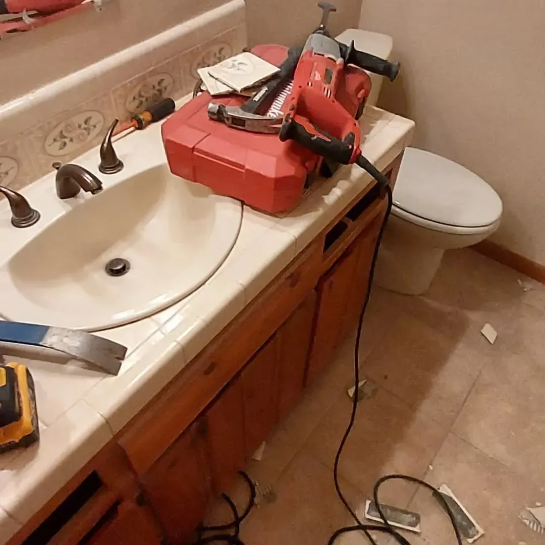 Bathroom renovation in progress with tools on countertop; sink, toilet, and cabinets visible.