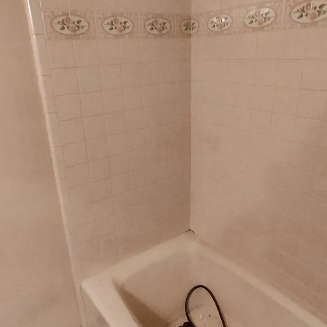 Corner of a bathroom with a white bathtub and tan tiled walls with a decorative border.