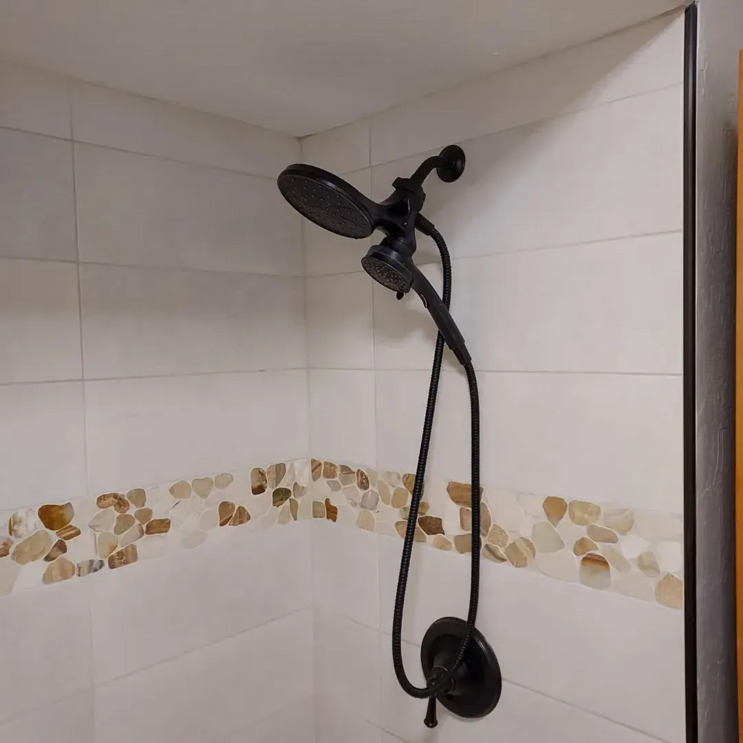 Black shower head with handheld sprayer, white and stone tile wall.