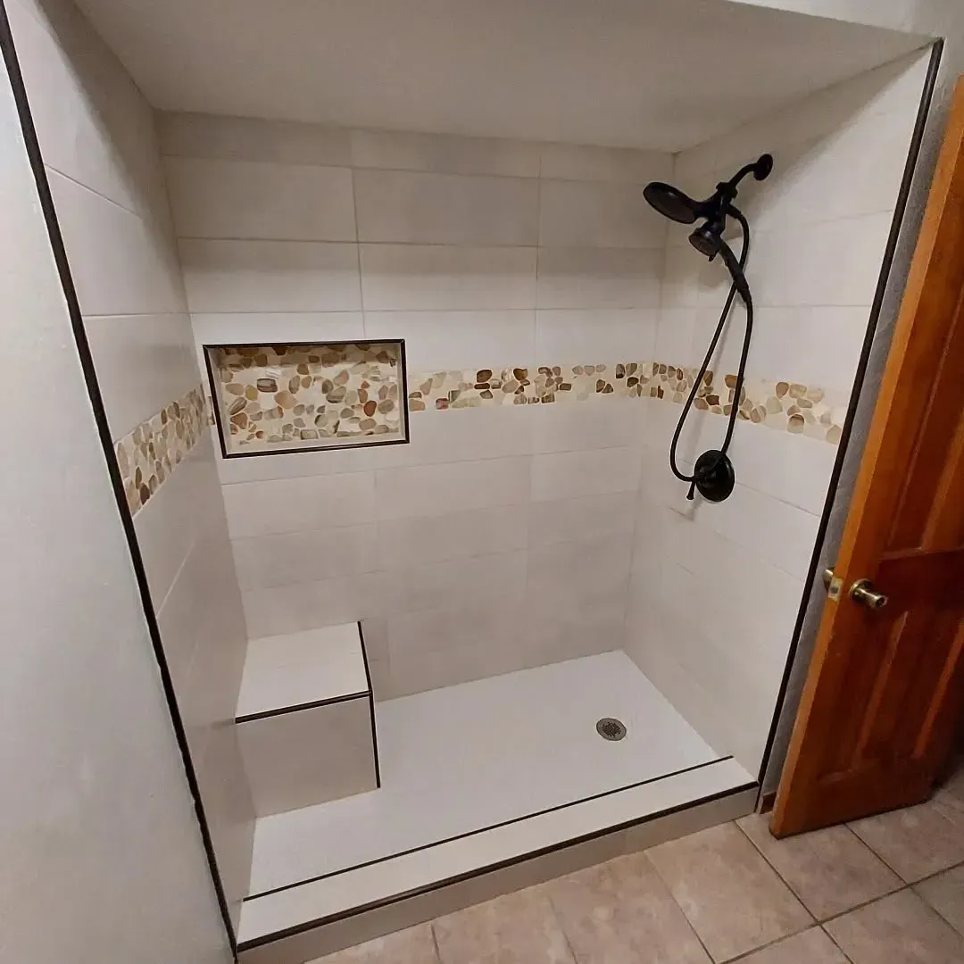Accessible shower with white walls, stone accent, built-in seat, and black fixtures.