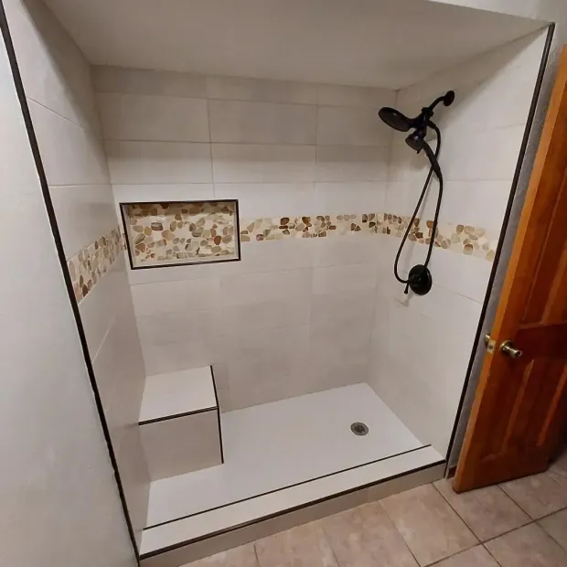 Accessible shower with white walls, stone accent, built-in seat, and black fixtures.