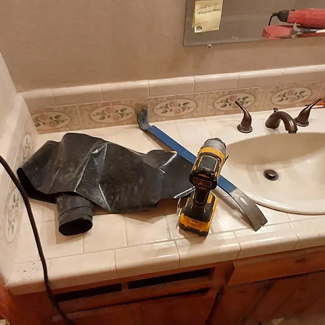Bathroom sink counter with tools and a black drain pipe.