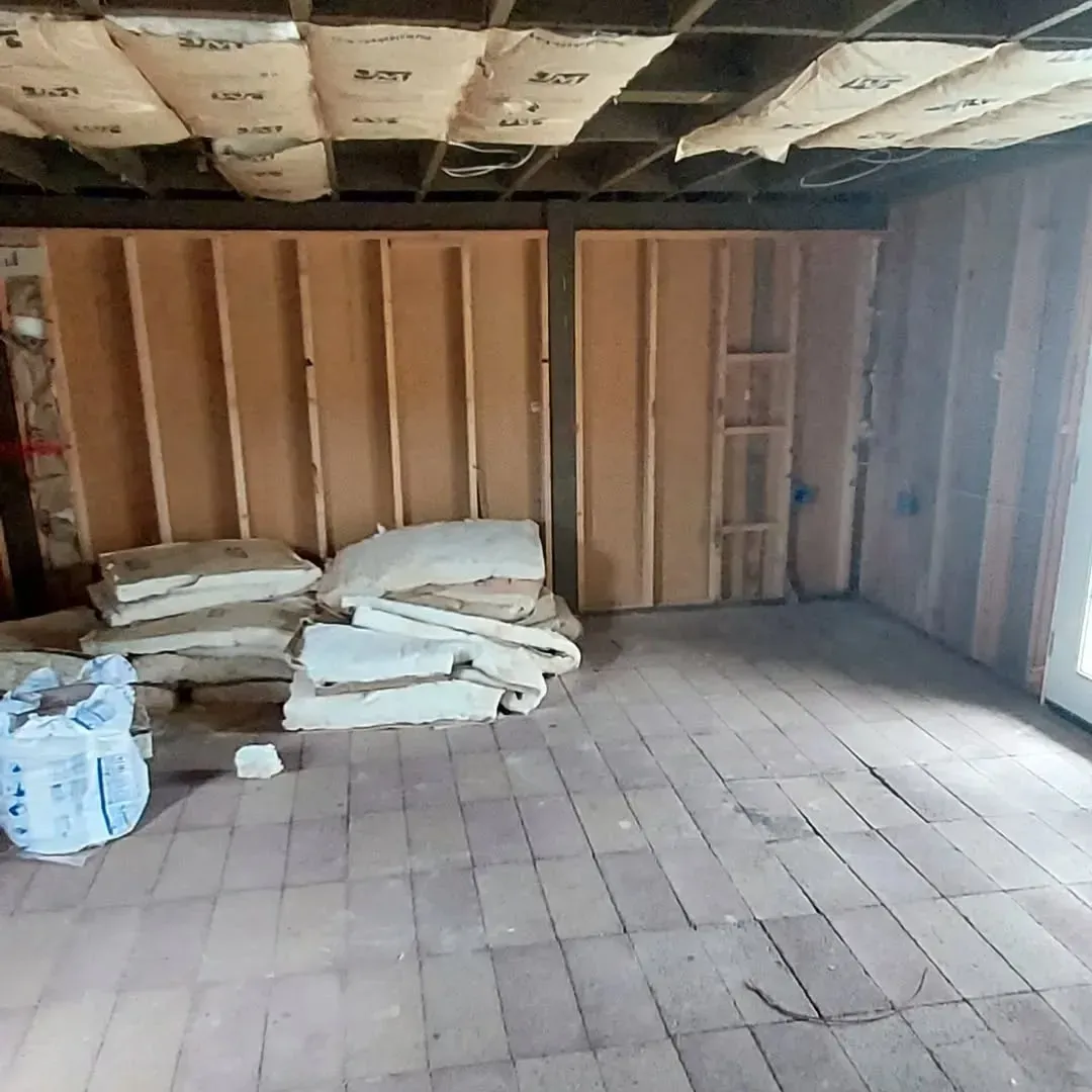Room under construction with wood framing, exposed ceiling insulation, and insulation bundles on the floor.