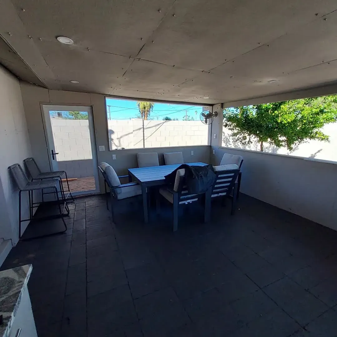 Outdoor dining area with a table, chairs, and cushions, under a covered patio.