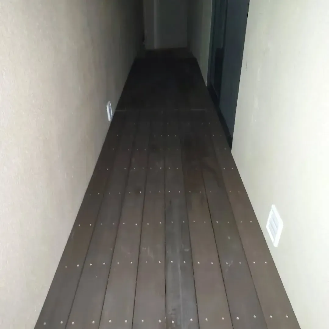 Narrow hallway with dark brown wooden flooring, beige walls, and white vents.