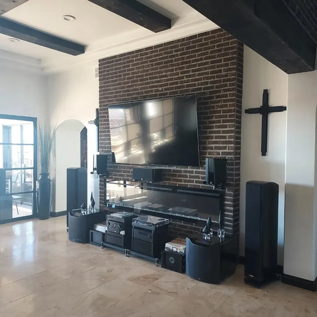 Living room with a brick accent wall, TV, and sound system. Black cross on the wall.
