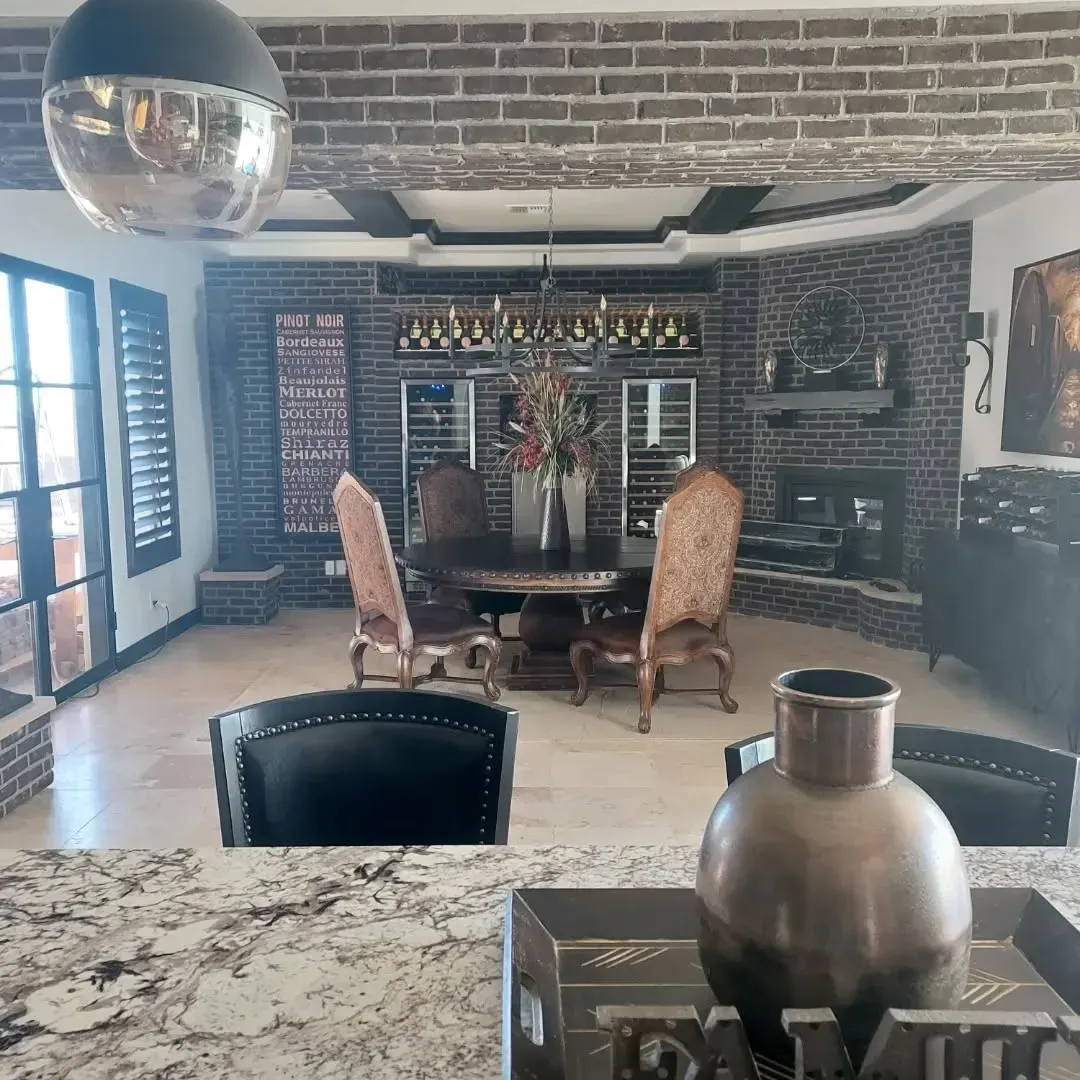 Dining room with brick accents, wooden beams, chandelier, table, chairs, and a fireplace.