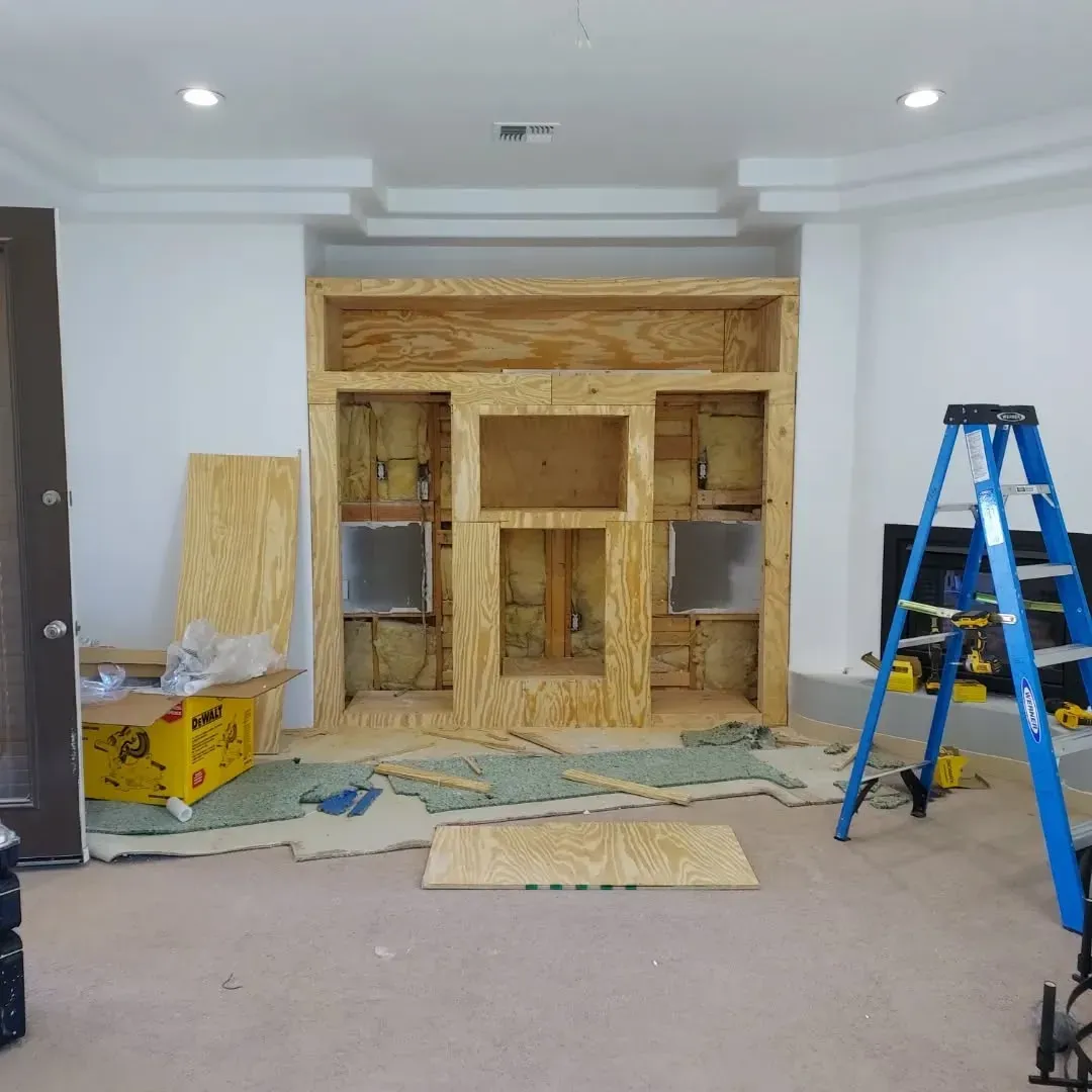 Construction of a wooden entertainment center in a room. A ladder and building materials are present.