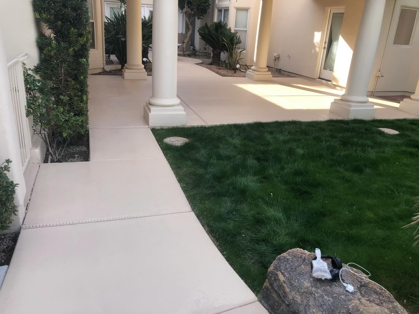 Sidewalk with pillars alongside a grassy area, leading to a building entrance.