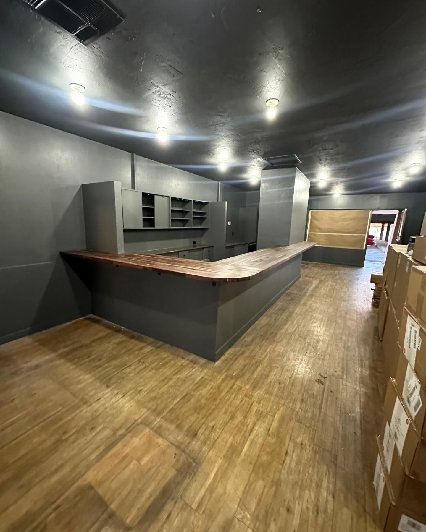 Empty interior with gray walls, a wooden bar, and light-colored wood flooring.