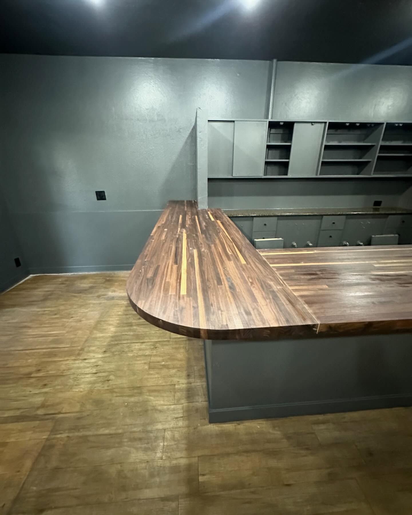 A dark wood bar with a curved front in a gray-walled interior, cabinets visible.