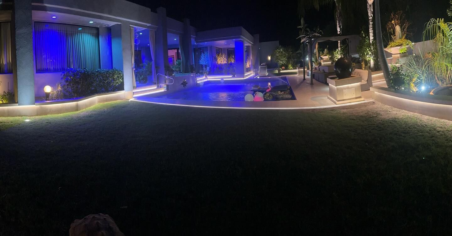 Night view of a house with blue lights, pool, and lawn.
