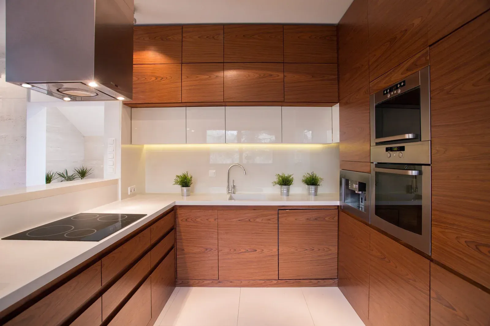 Modern wood-toned kitchen with white countertops, stainless steel appliances, and bright lighting.