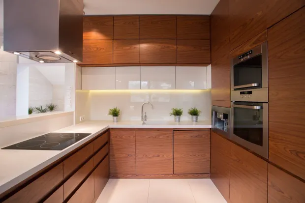 Modern wood-toned kitchen with white countertops, stainless steel appliances, and bright lighting.