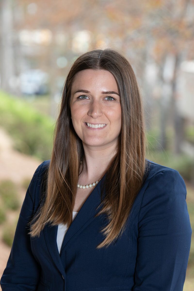 A woman in a blue jacket and pearl necklace is smiling for the camera.