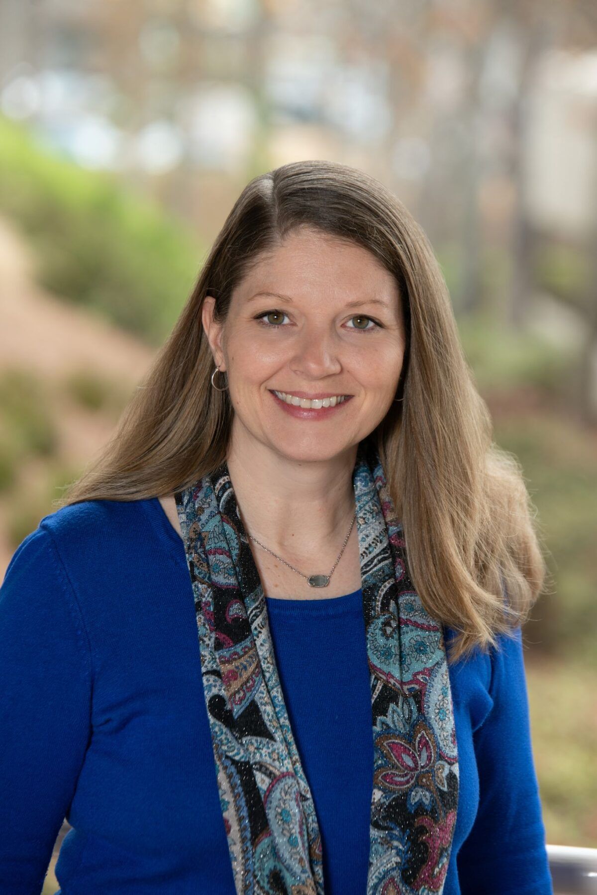 A woman in a blue shirt and scarf is smiling for the camera.