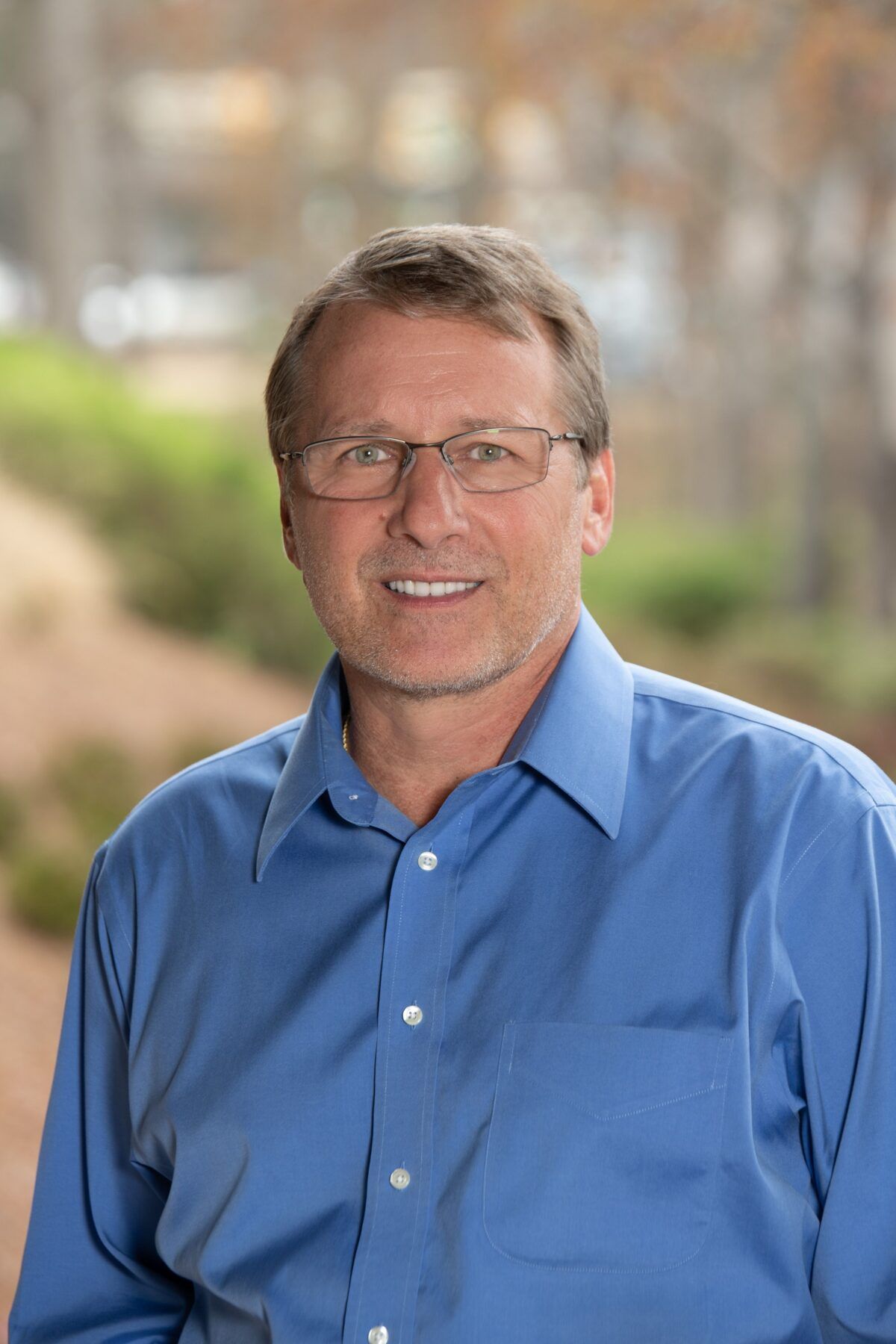 A man wearing glasses and a blue shirt is smiling for the camera.