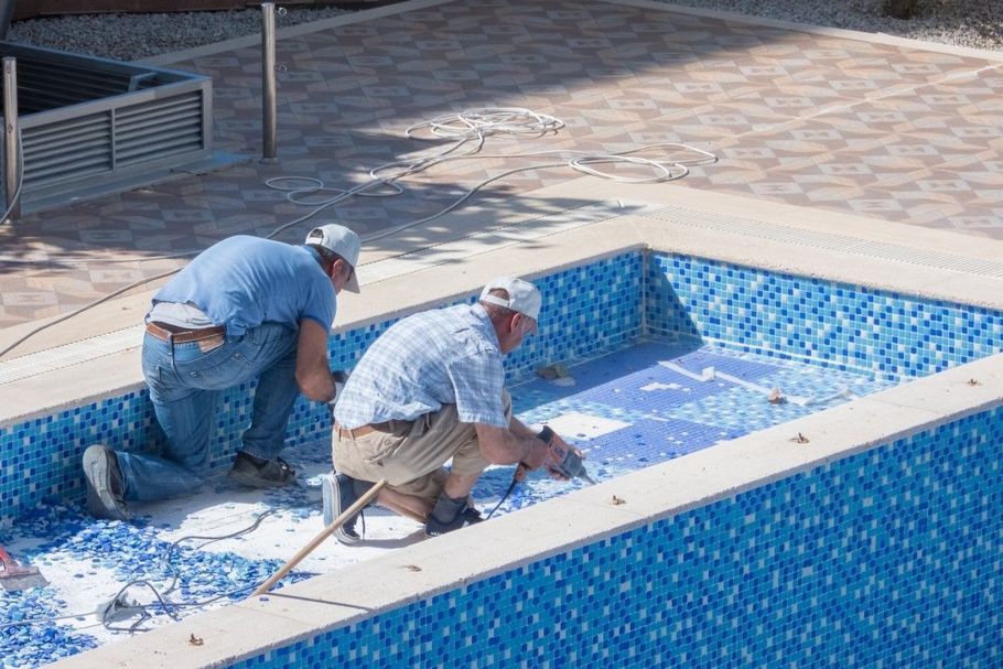 Workers repairing tiles in a swimming pool.