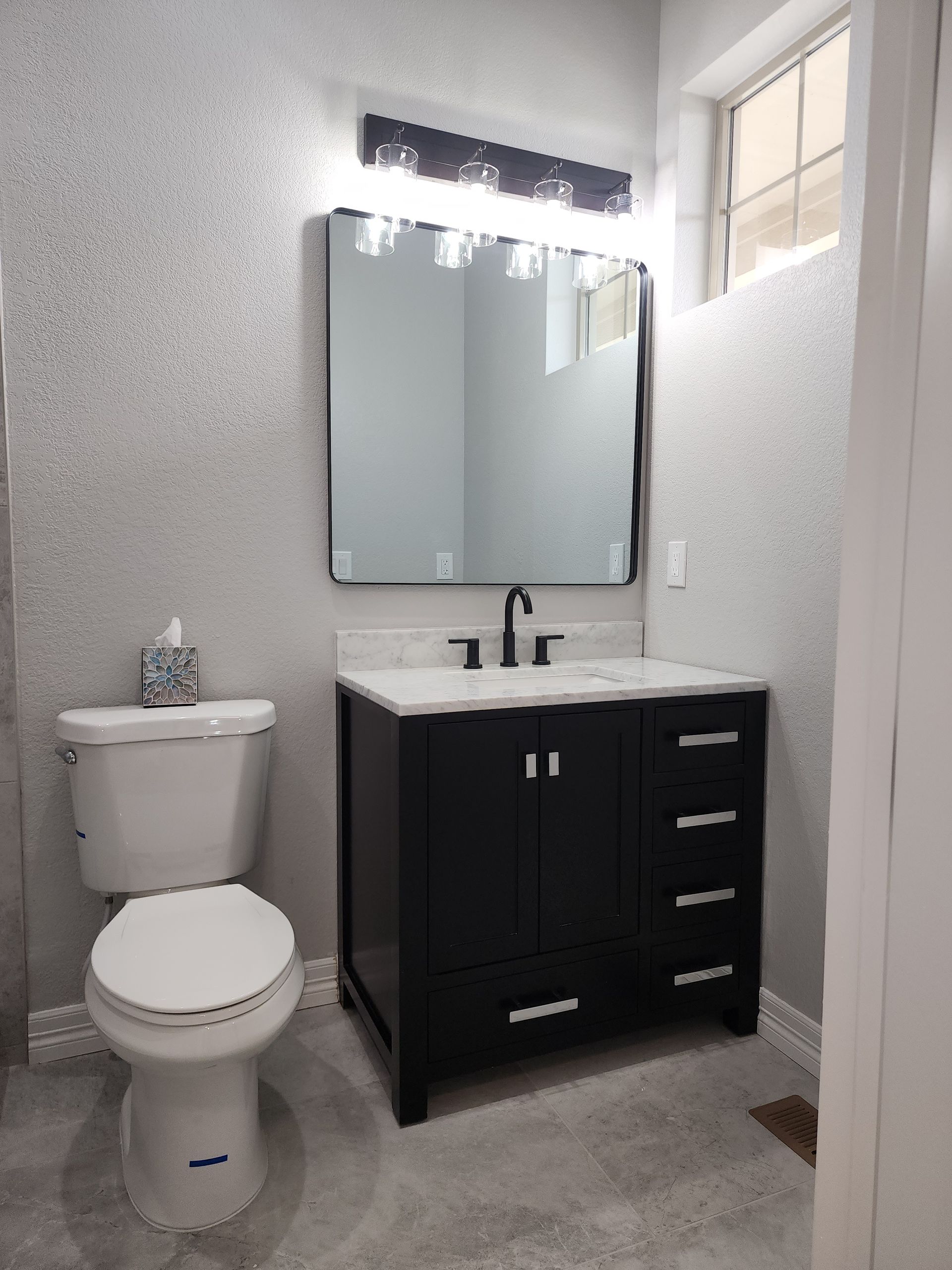Small bathroom with black vanity, mirror, toilet, and silver-textured walls.