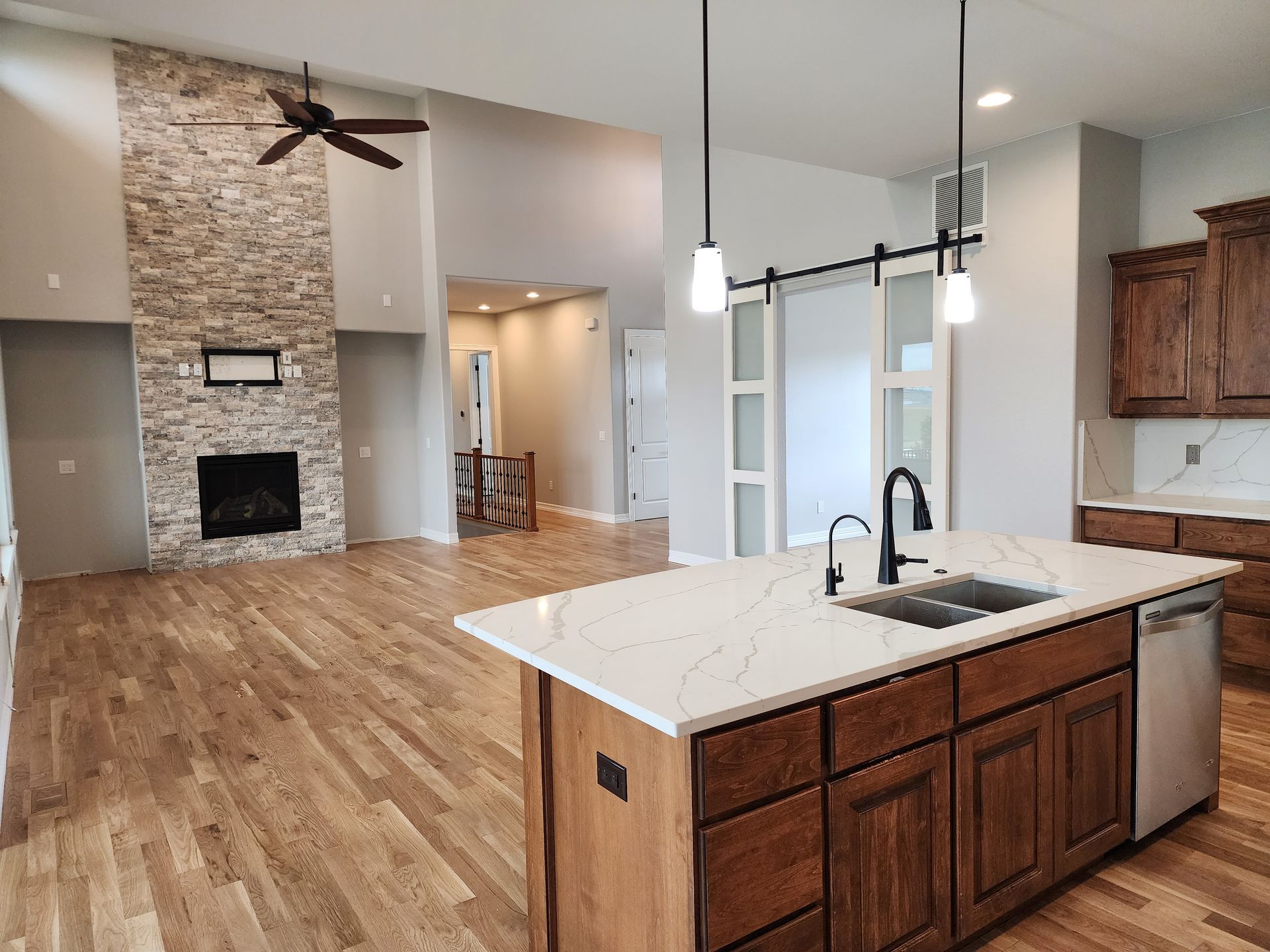 Spacious kitchen with island, stone fireplace, light wood floors, and dark brown cabinets.