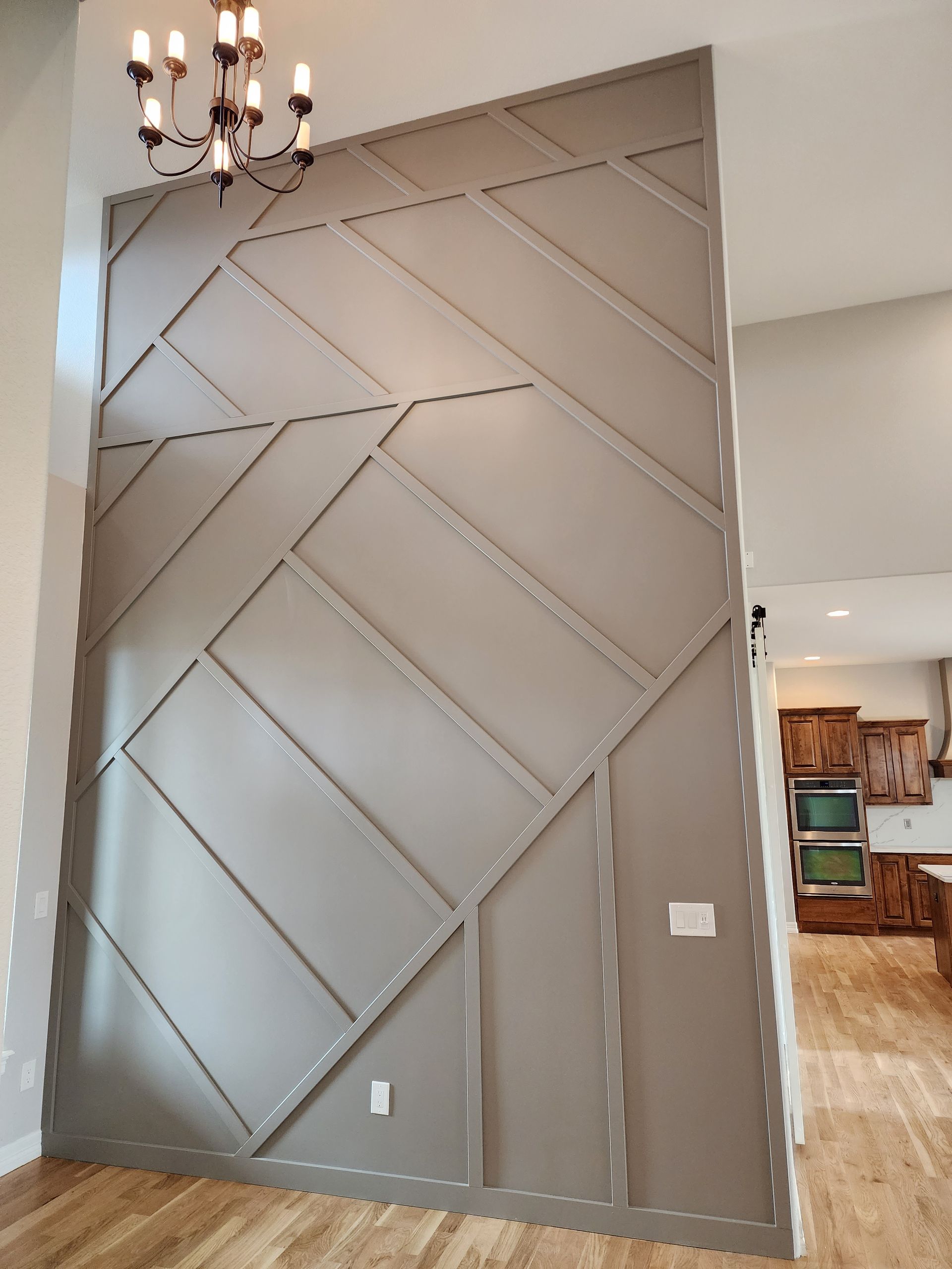 Gray accent wall with geometric molding, a chandelier, and a glimpse of a kitchen.