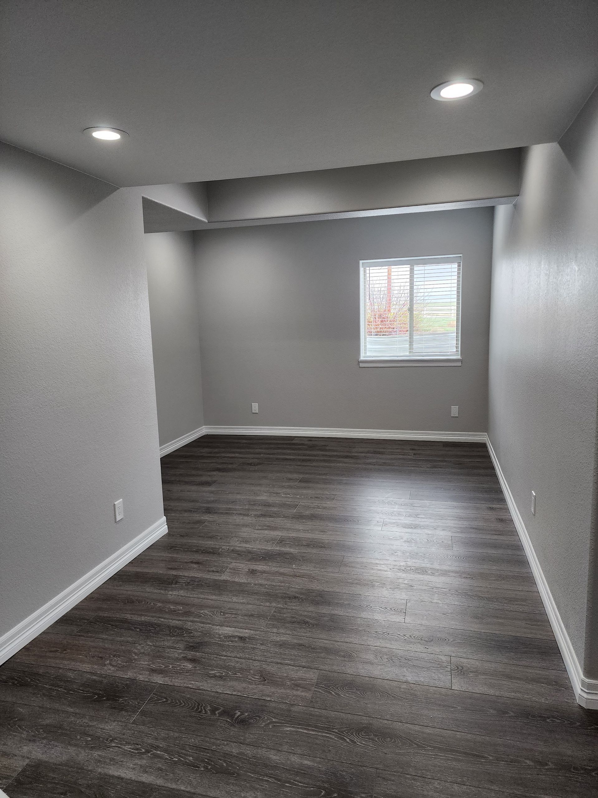 Empty room with gray walls, dark floor, window, and recessed lighting.