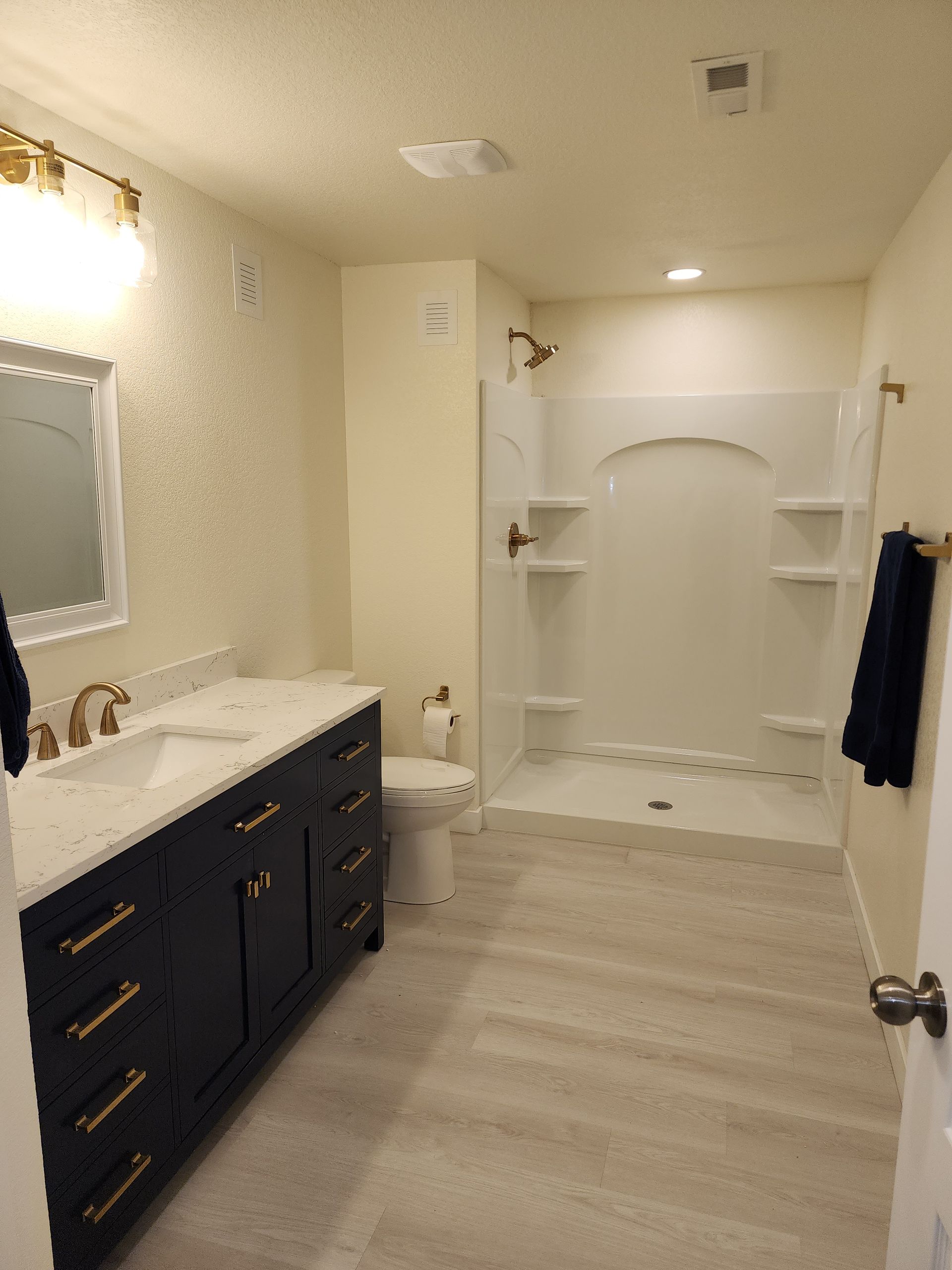 Modern bathroom with dark blue vanity, white countertops, and a shower stall.