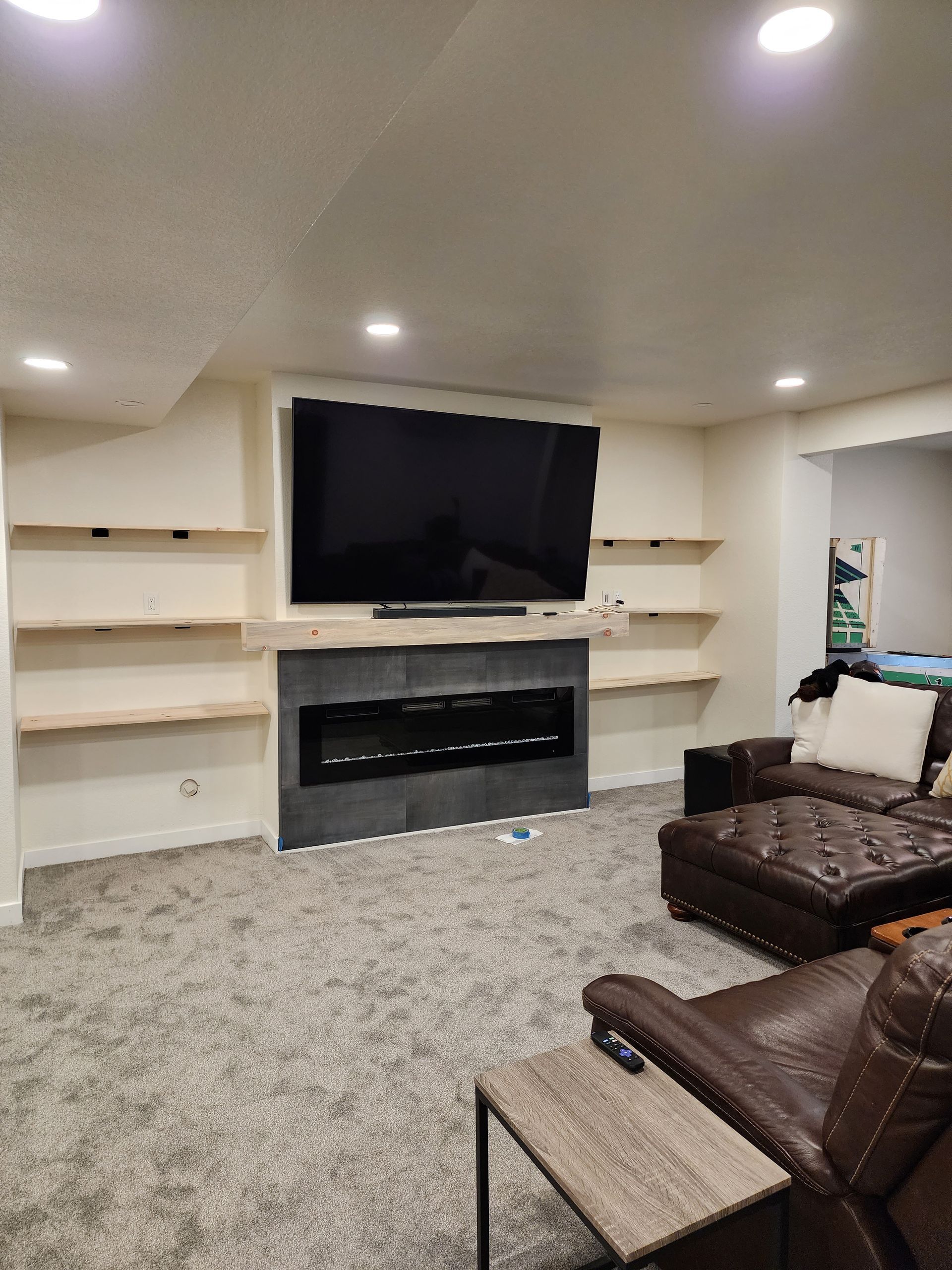 Living room with TV, fireplace, shelves, brown leather furniture, and gray carpet.