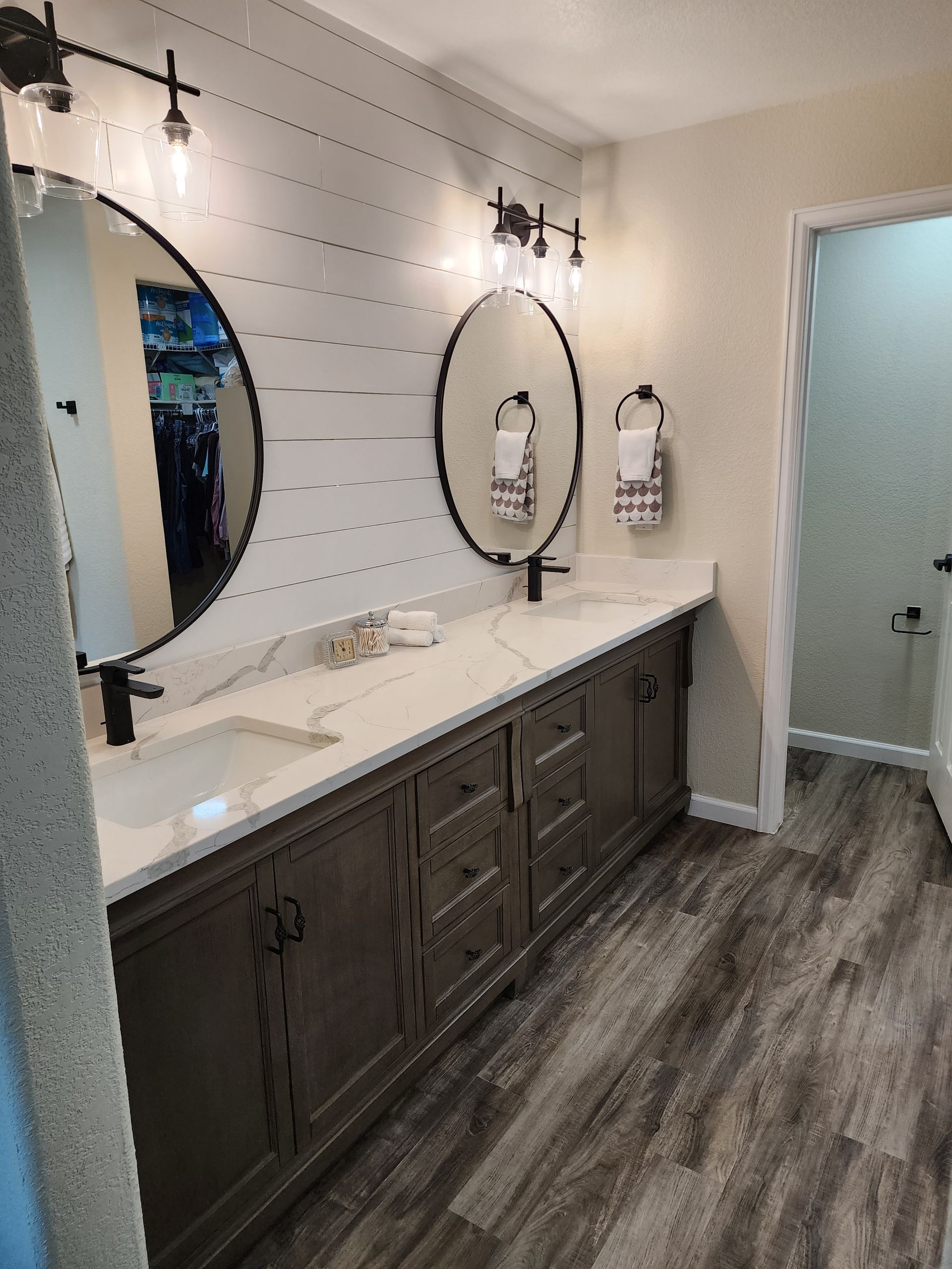 Bathroom with a gray vanity, white countertop, oval mirrors, and shiplap wall.