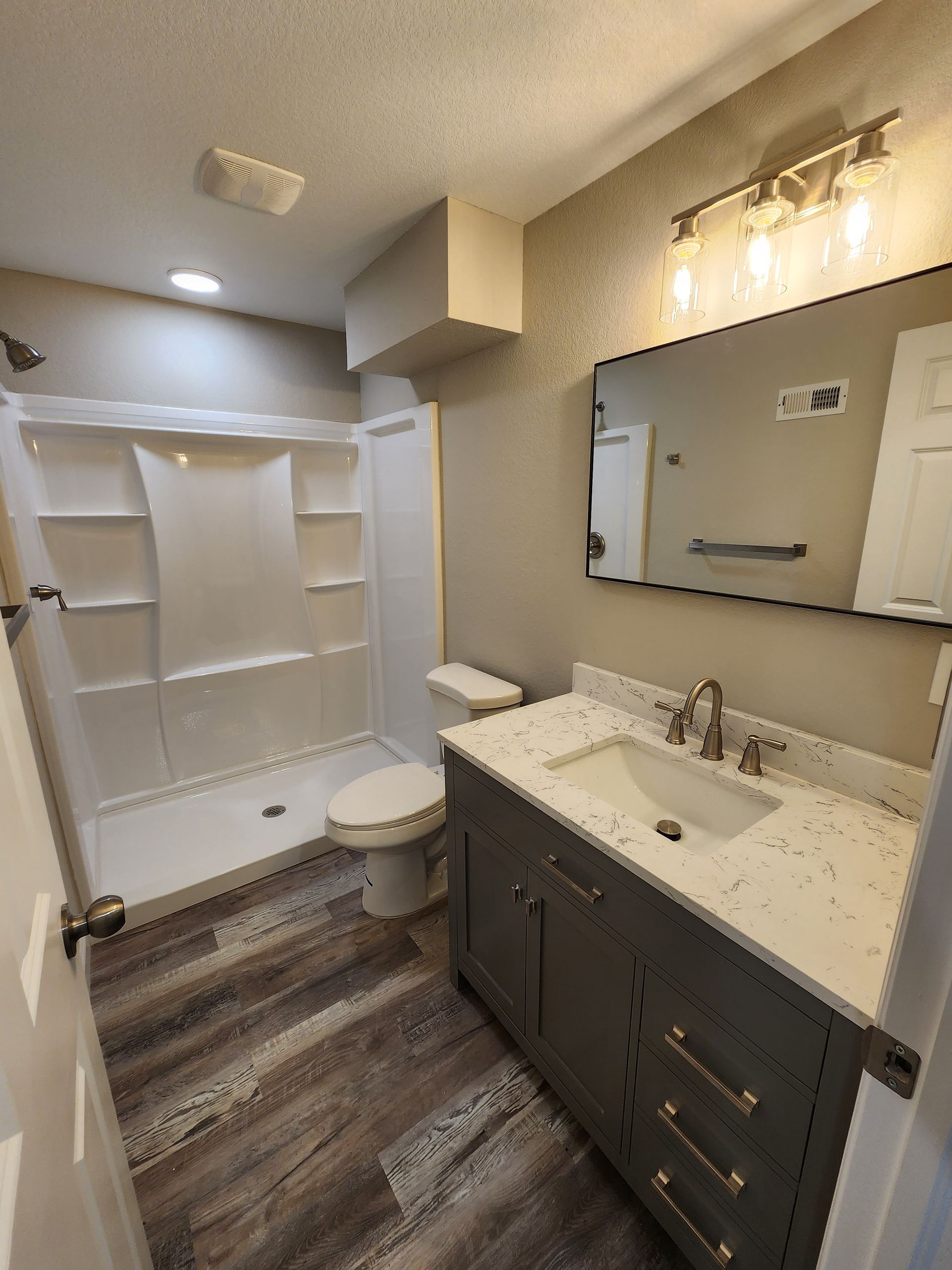 Bathroom with a white shower, grey vanity, and wood-look floor.