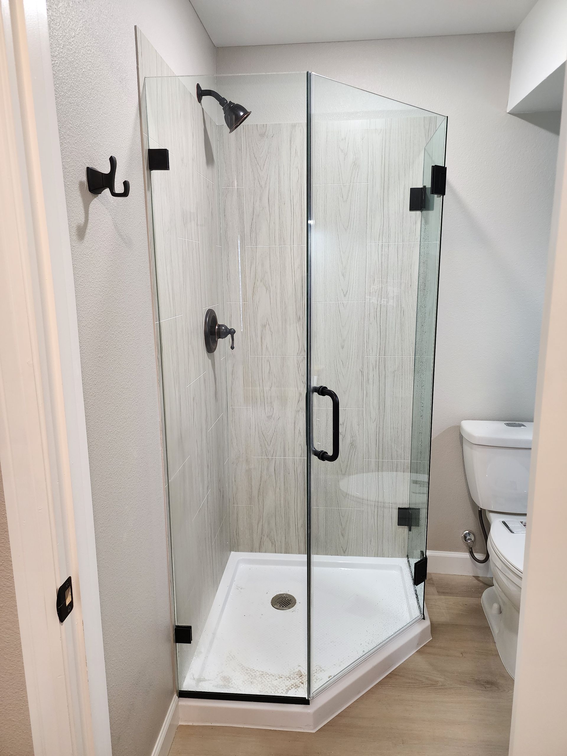 Corner shower with glass doors, black hardware, and gray tile.