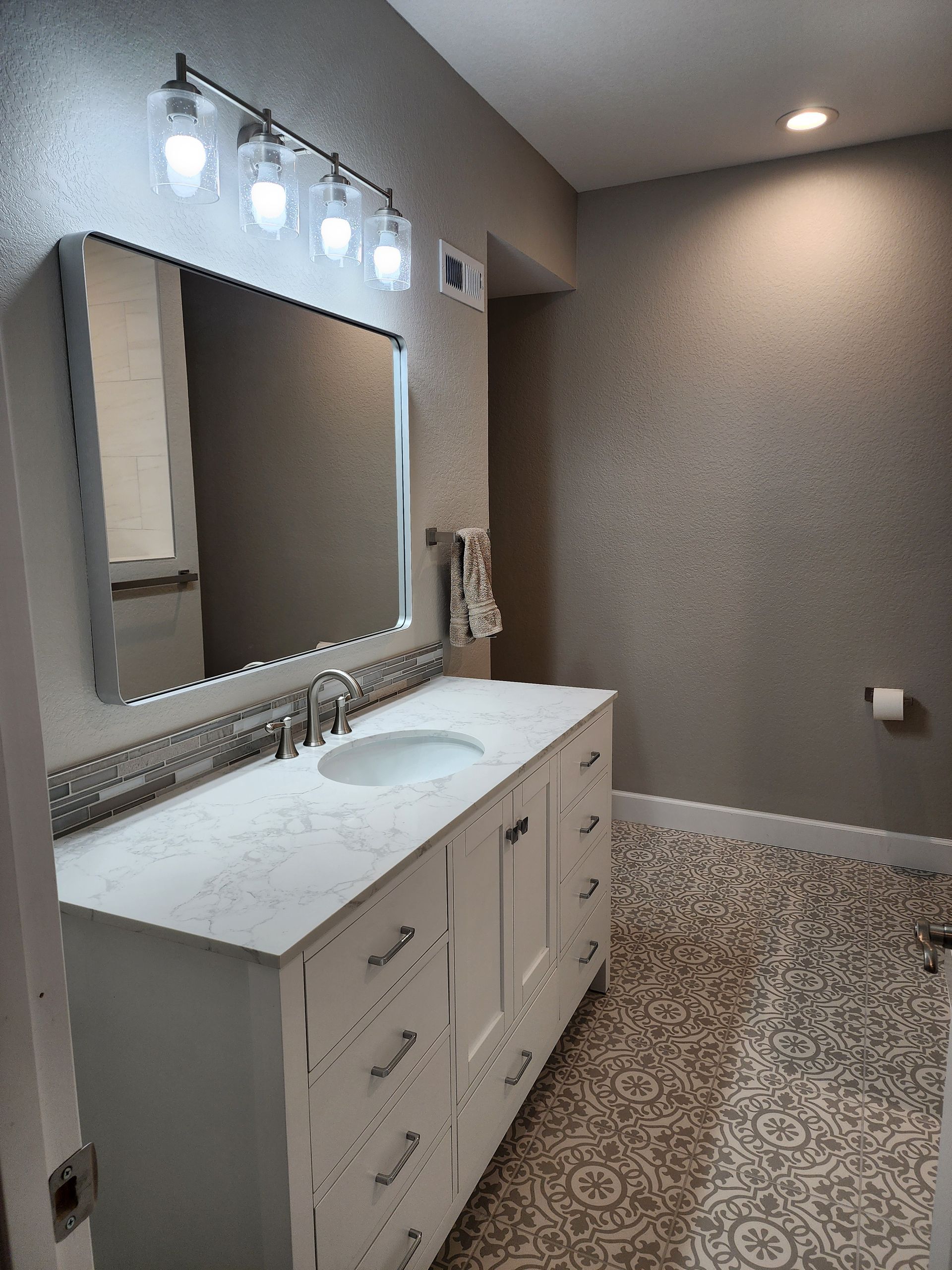Bathroom with white vanity, marble countertop, and decorative tile floor. Gray walls with textured finish.