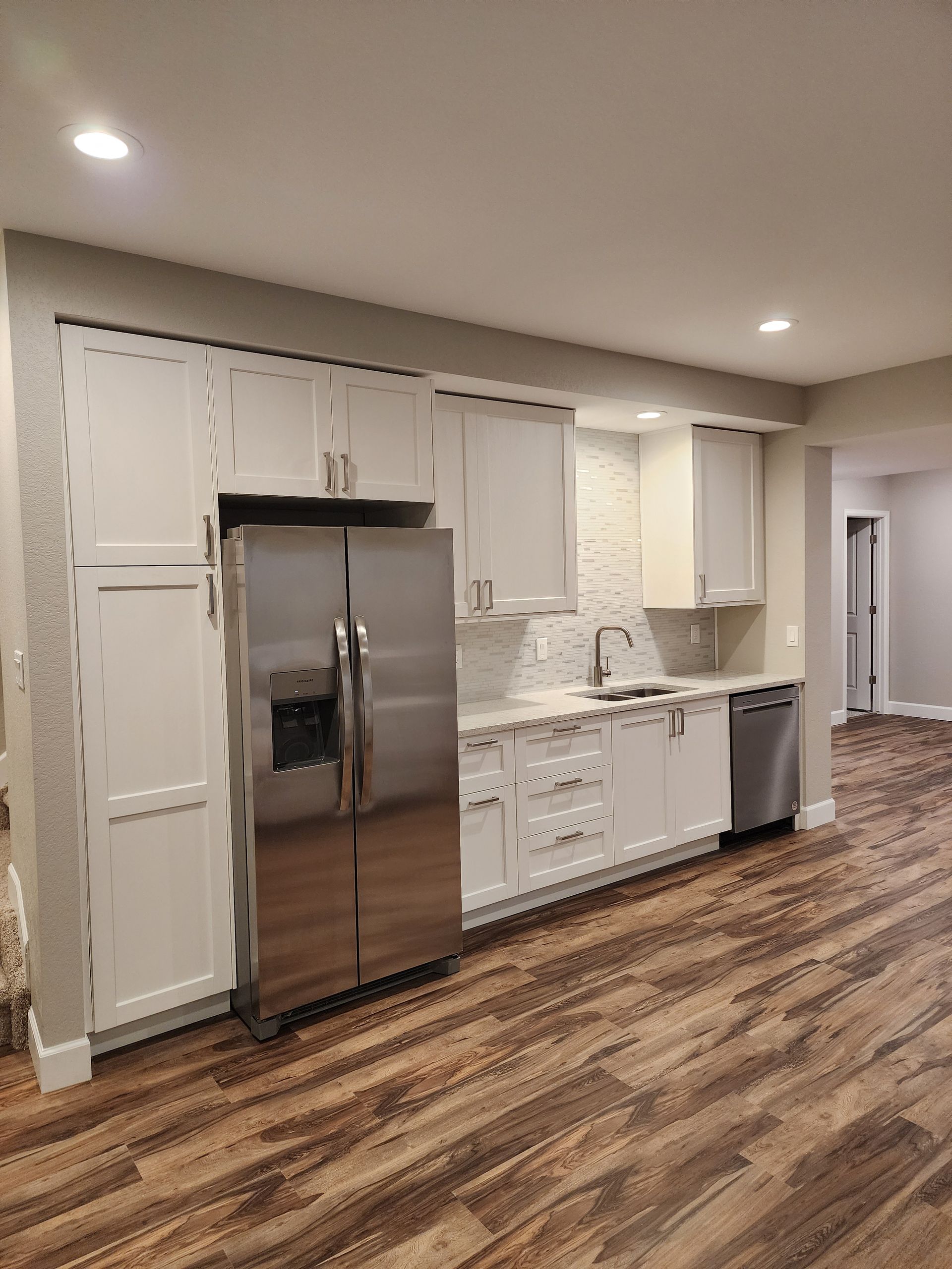 White kitchen with stainless steel appliances on wood-look floor.