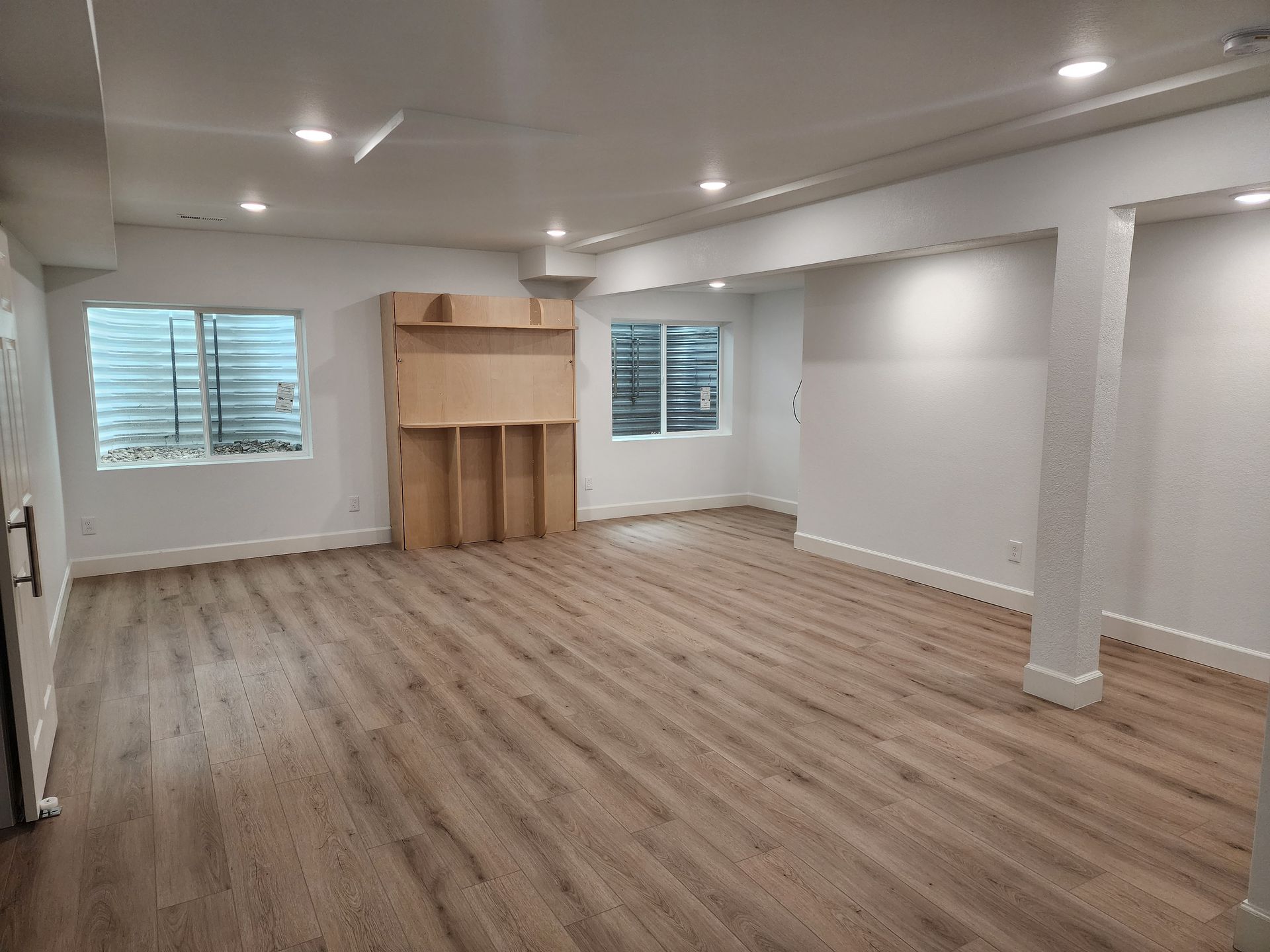 Spacious, empty room with wooden floor, white walls, and two small windows.