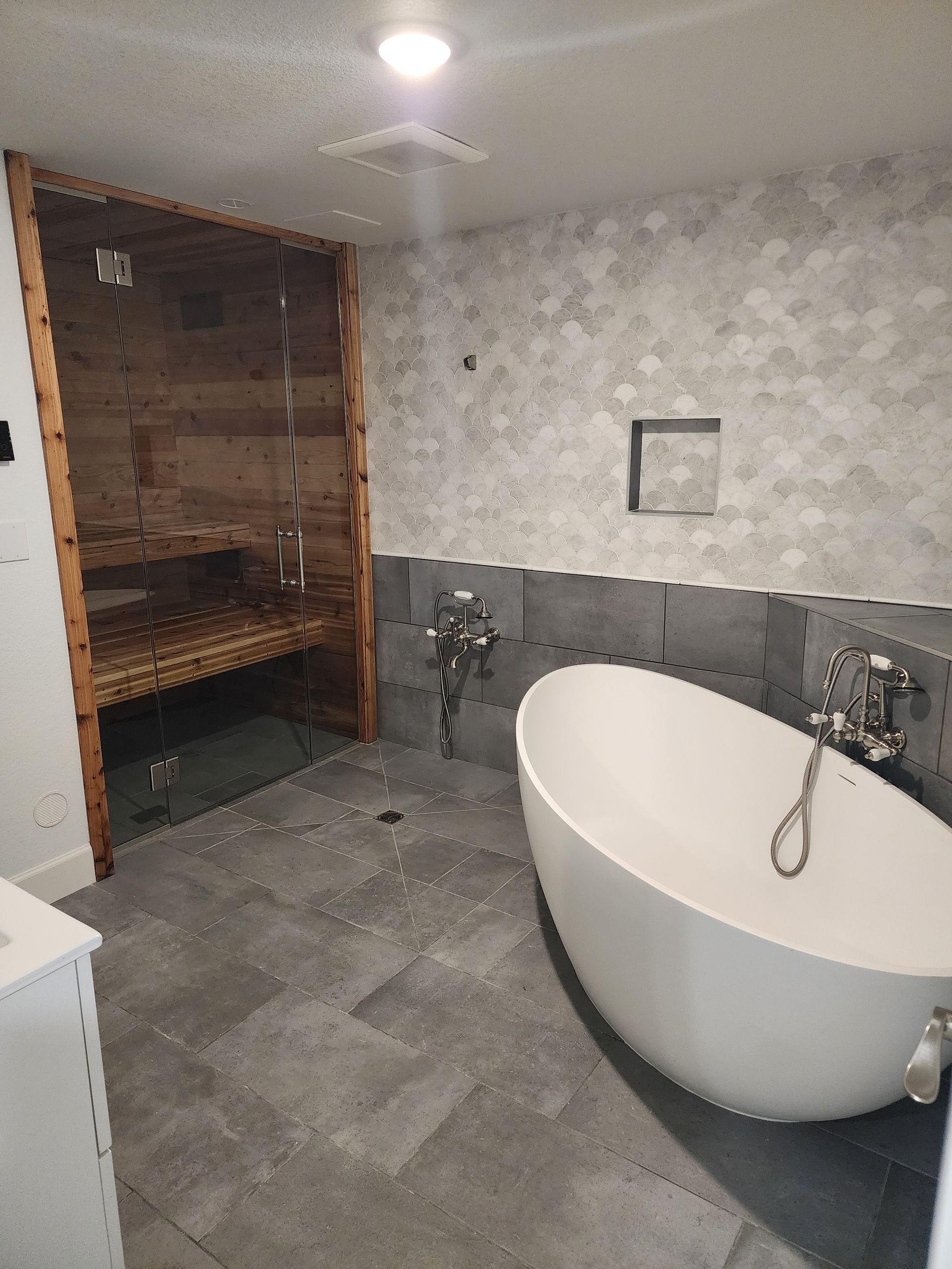 Modern bathroom with a sauna, oval tub, gray tile, and patterned walls.