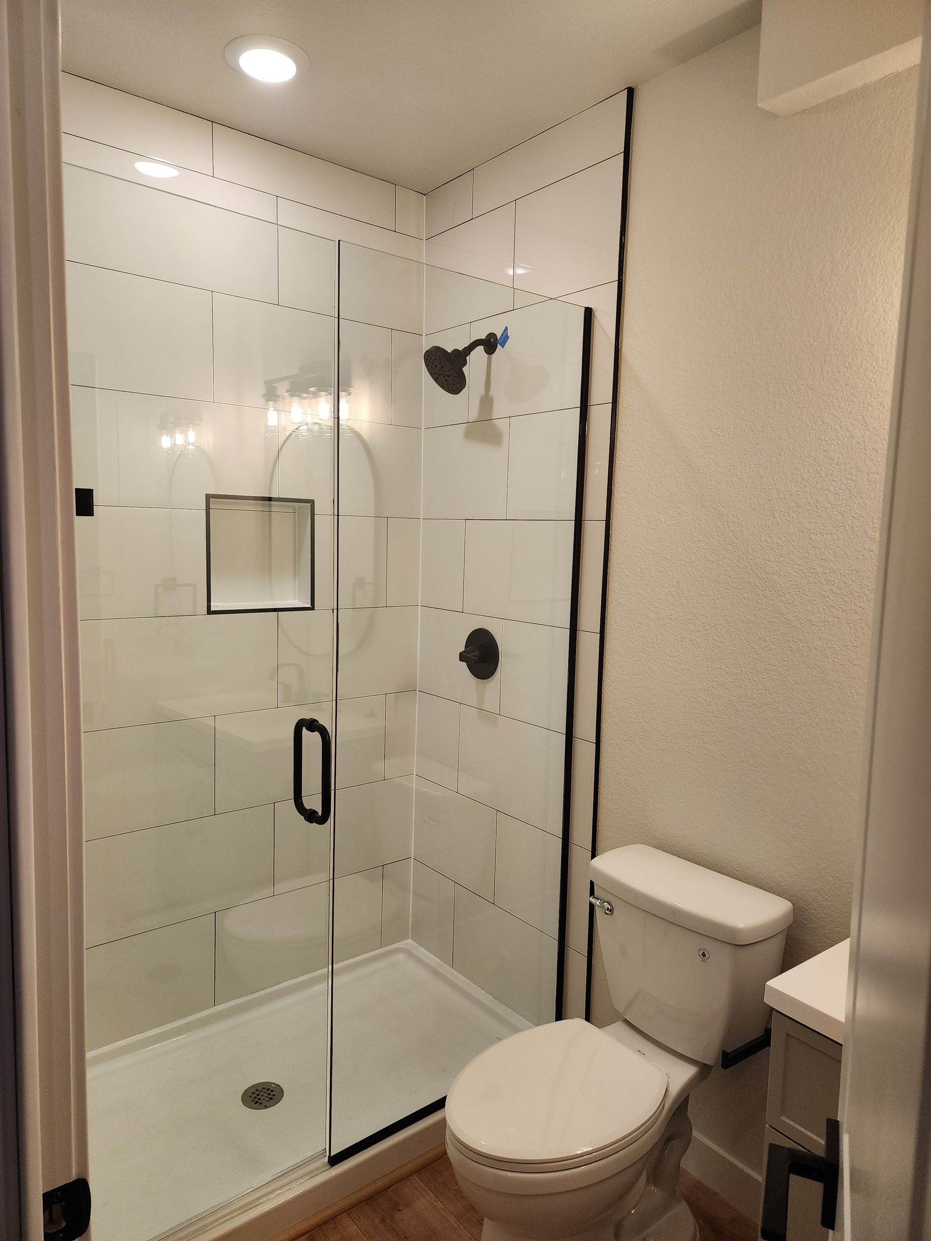 A small white bathroom with a glass shower, black fixtures, and a toilet.
