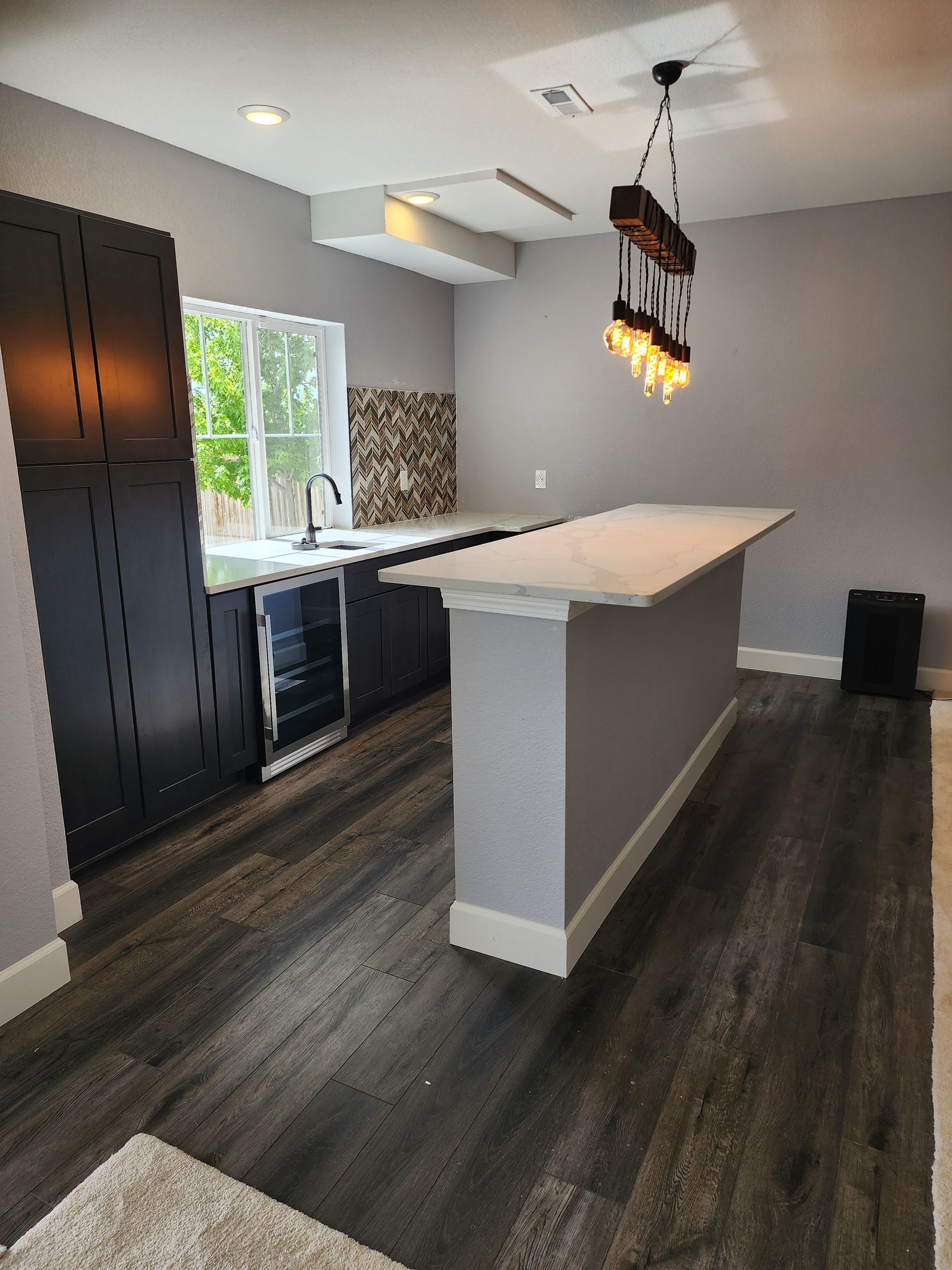 Modern kitchen with black cabinets, gray walls, and a white countertop island; dark wood flooring.
