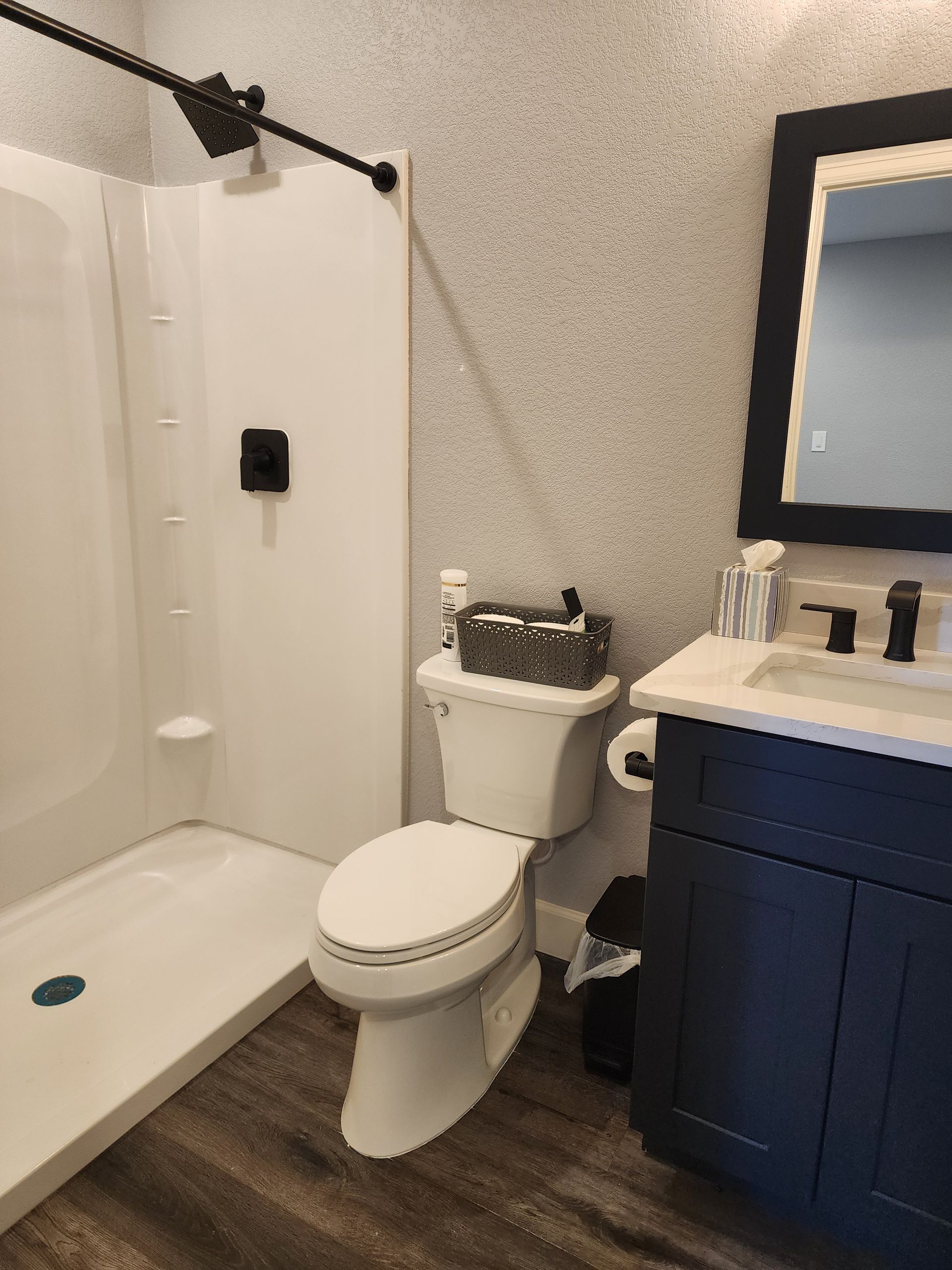 Small bathroom with a white shower, toilet, dark blue vanity, and speckled gray walls.