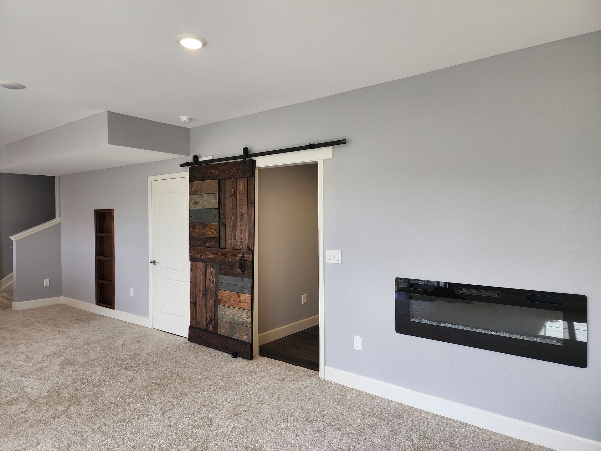 A room with a barn door, fireplace, gray walls, and beige carpet.