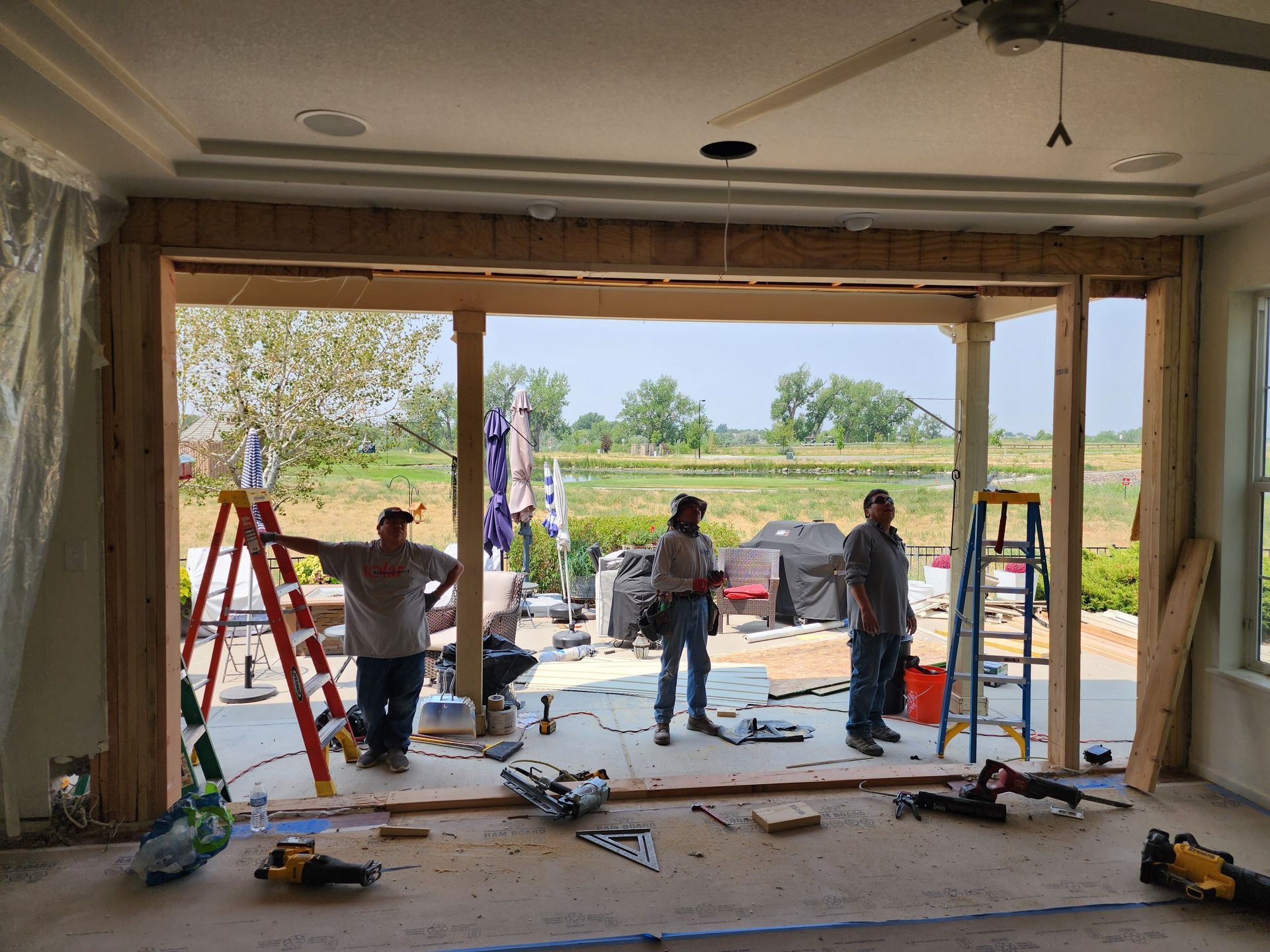 Construction workers at an open doorway, framing new patio door. Tools and materials strewn on the floor.
