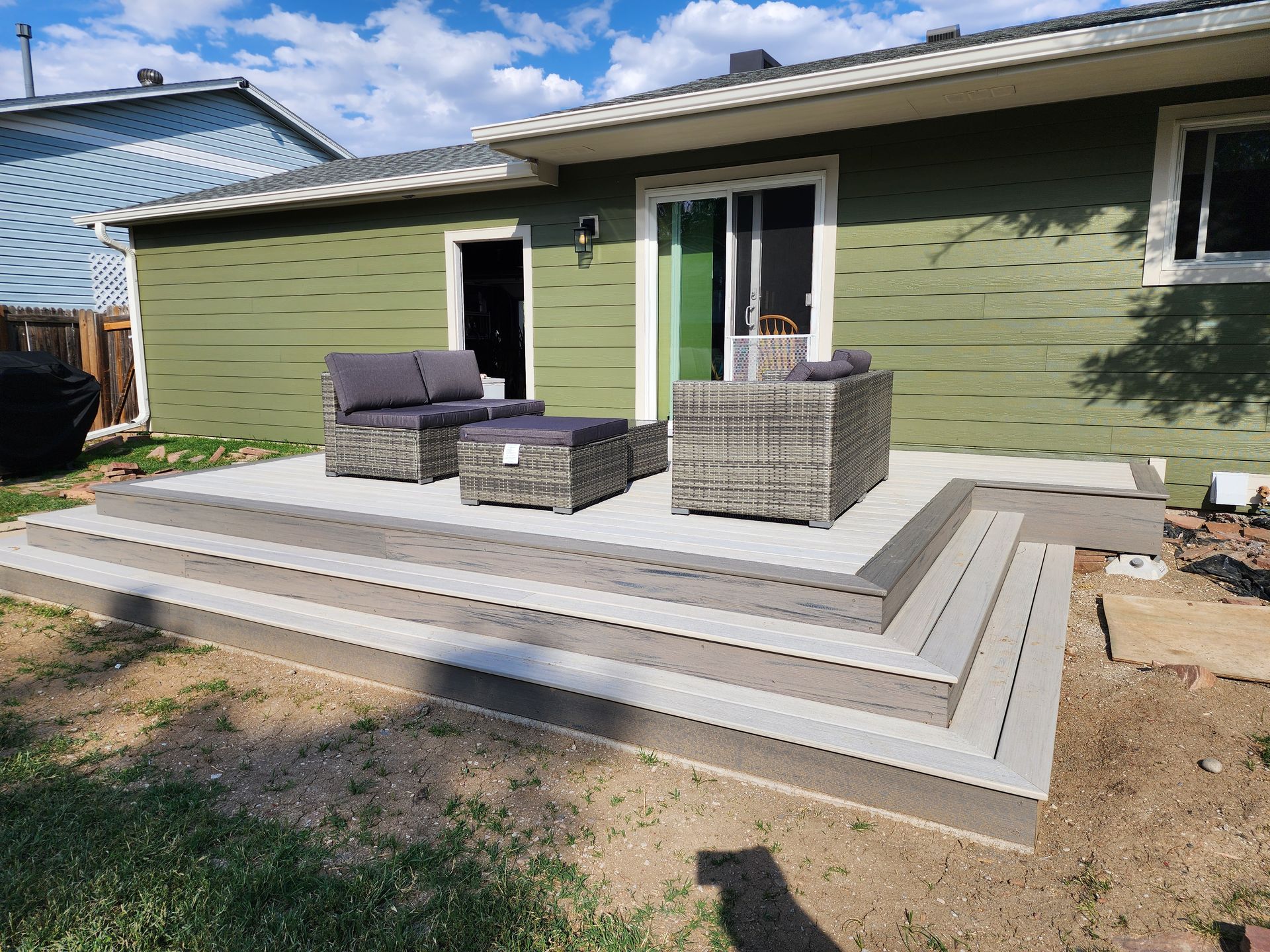 A gray composite deck with outdoor furniture sits outside a green house.