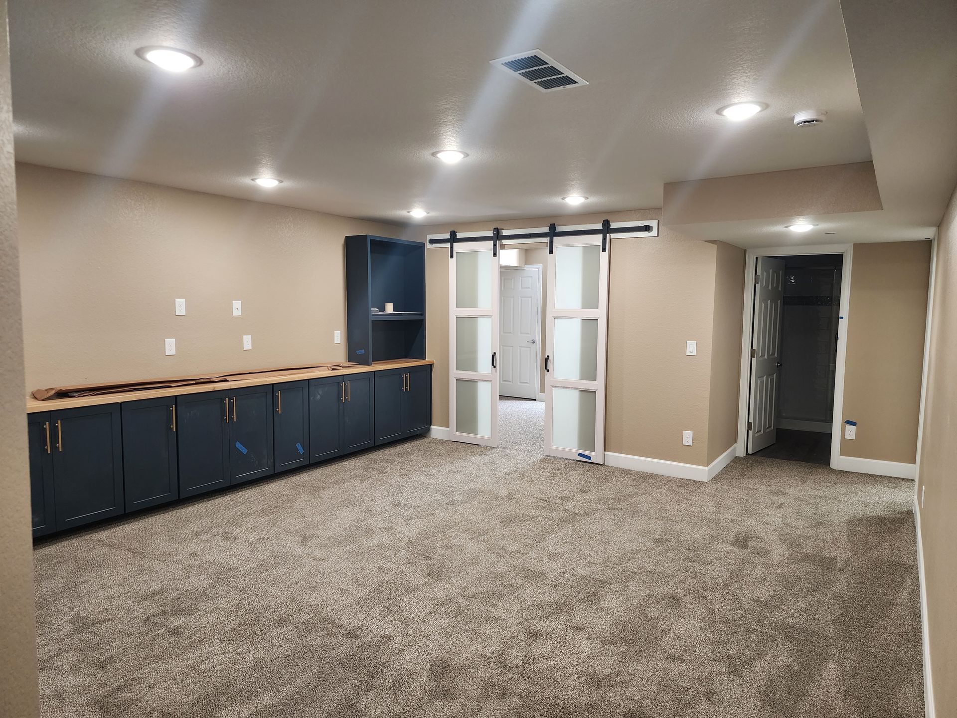 Basement room with blue cabinets, sliding doors, carpet, and recessed lighting.