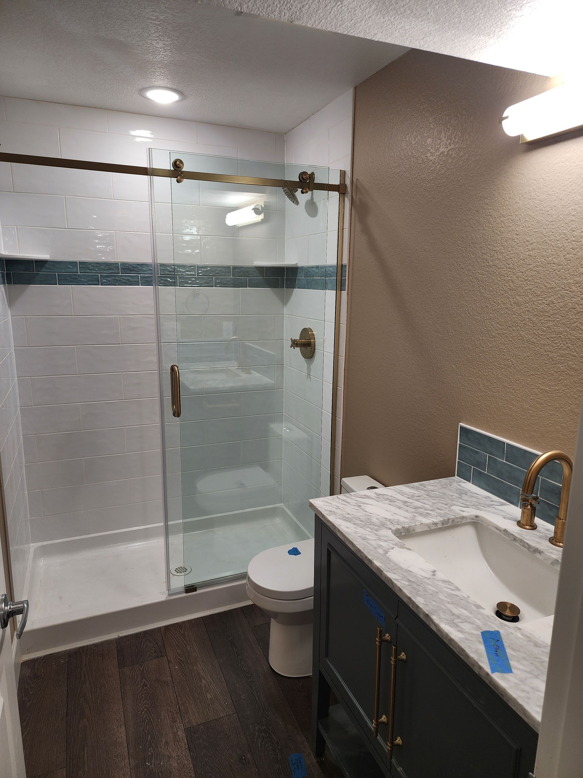 Bathroom with shower, toilet, vanity, and dark wood floor. Blue, white, and gold accents.