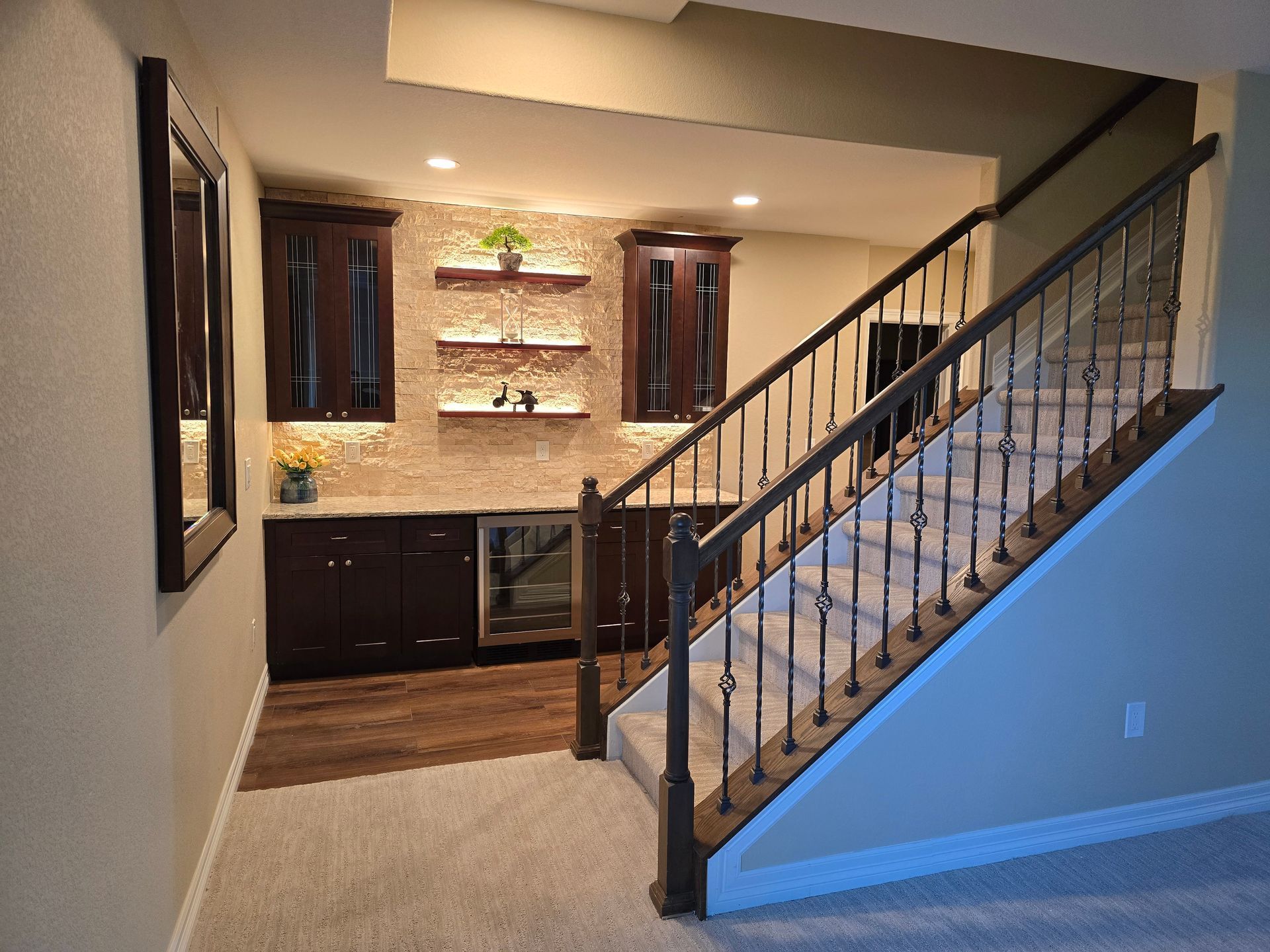 Finished basement with a bar, stairs, and cabinets. Dark wood, beige walls, and patterned backsplash.