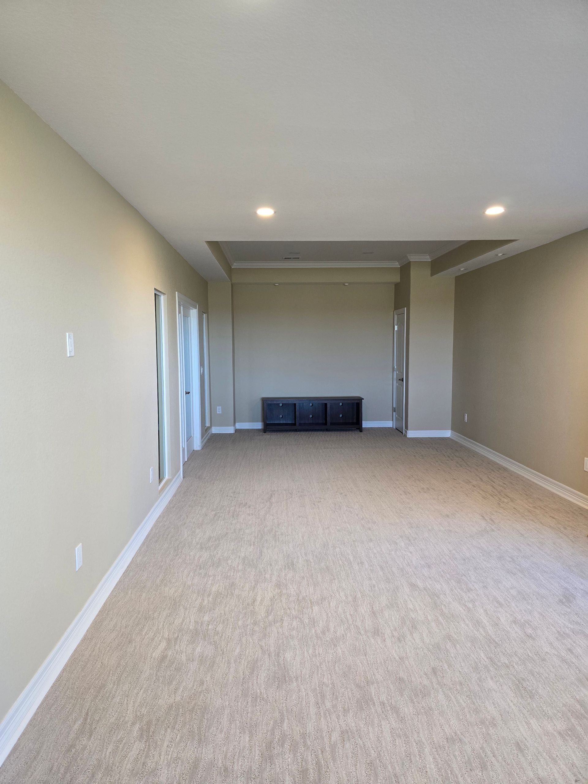Empty room with tan carpet, beige walls, and a built-in entertainment center.