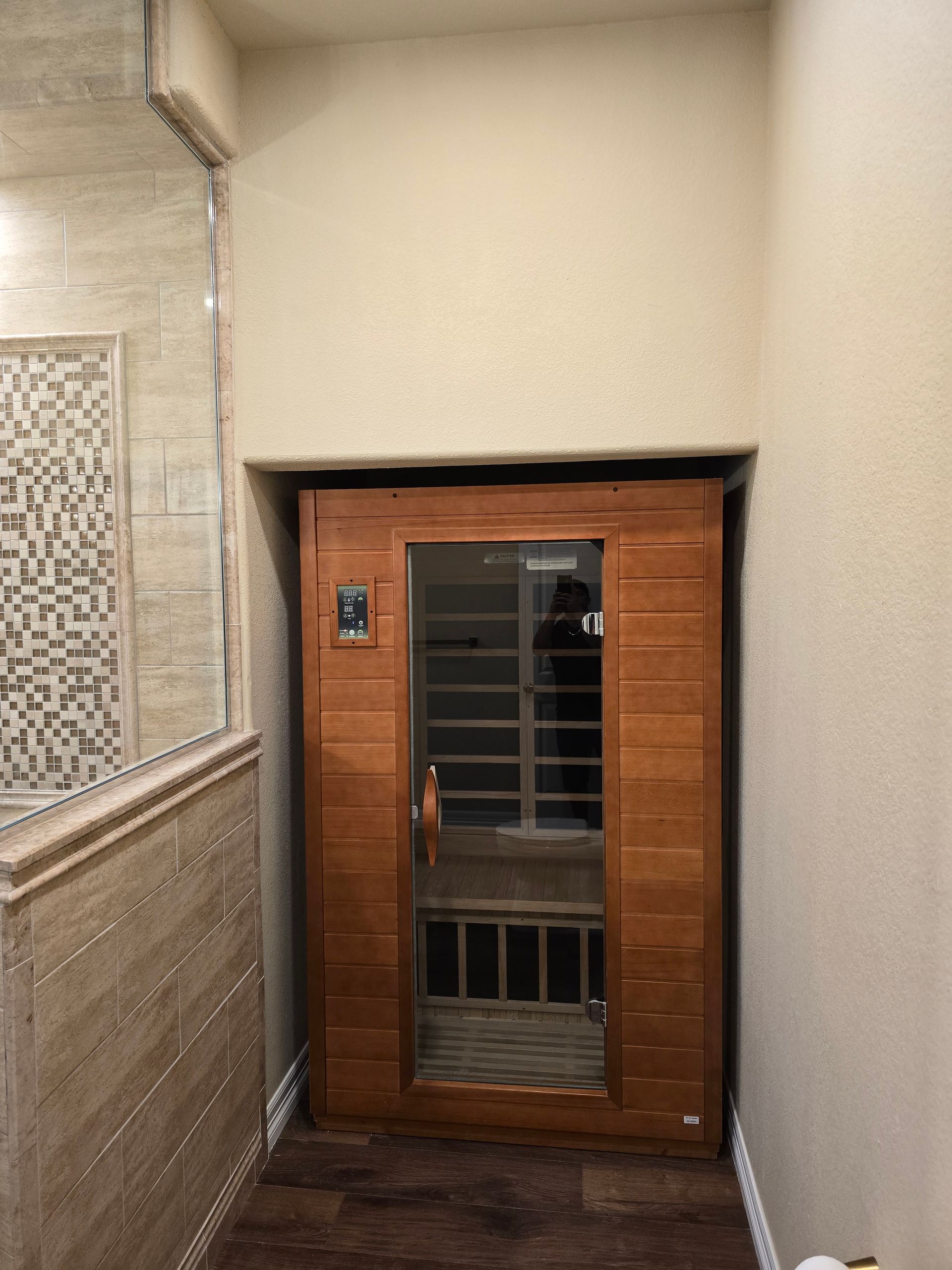Wooden sauna recessed in a bathroom alcove, next to a tiled shower.