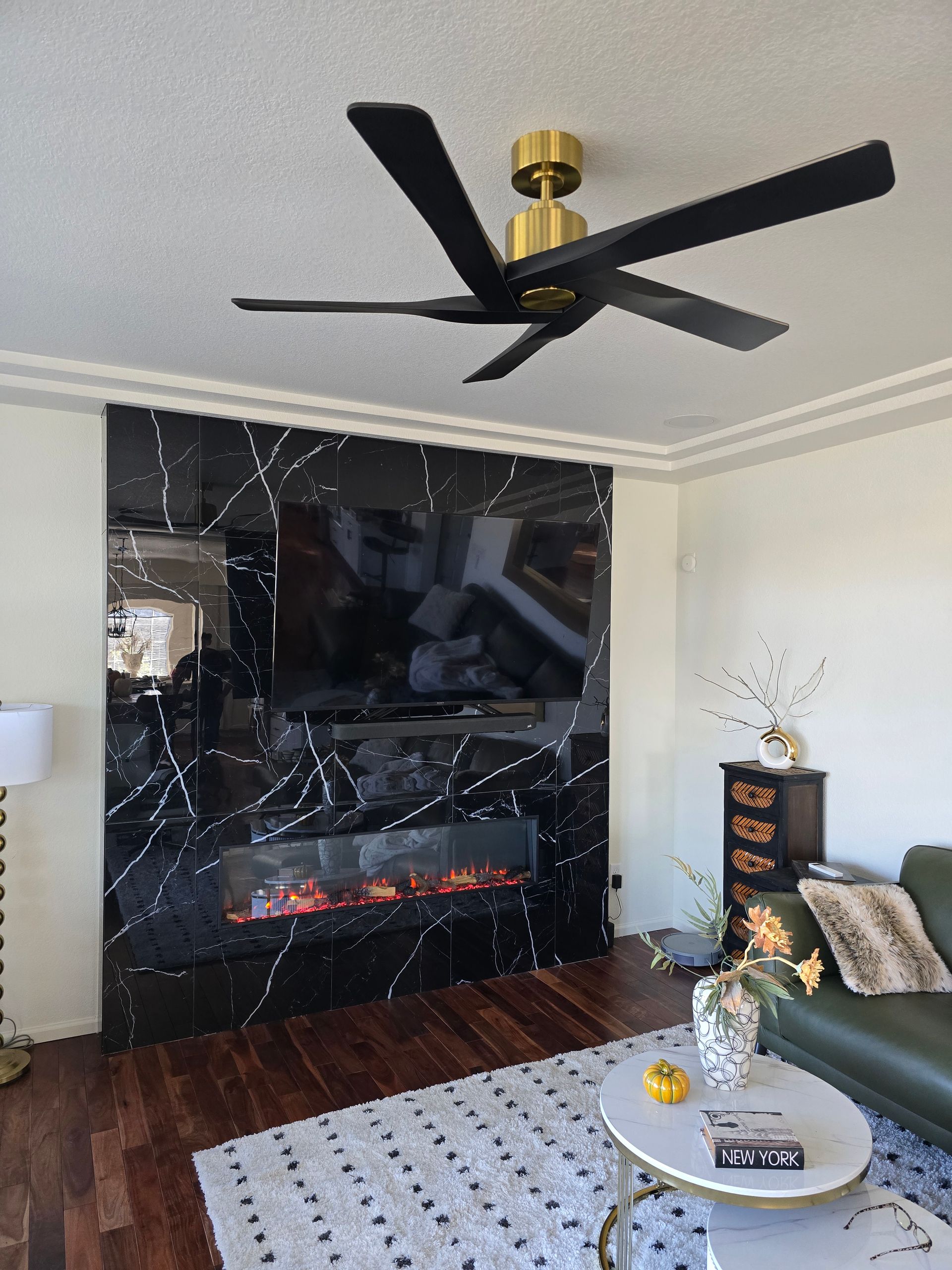 Living room with black marble fireplace and TV, gold and black ceiling fan, and a green sofa.