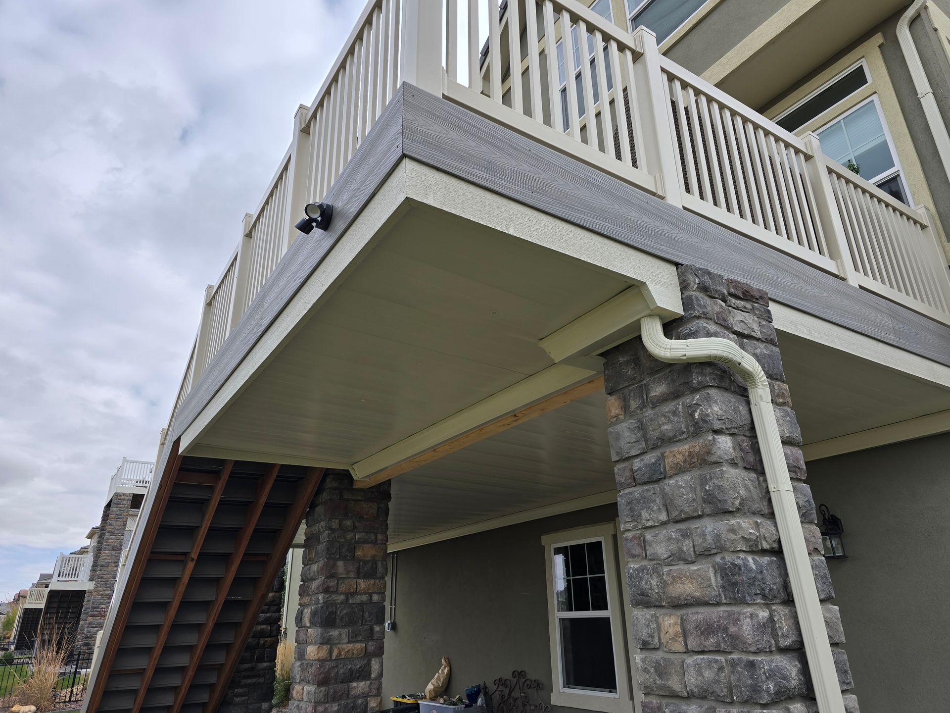 Low angle view of a two-story deck with stairs, supported by stone columns, and light beige railing.